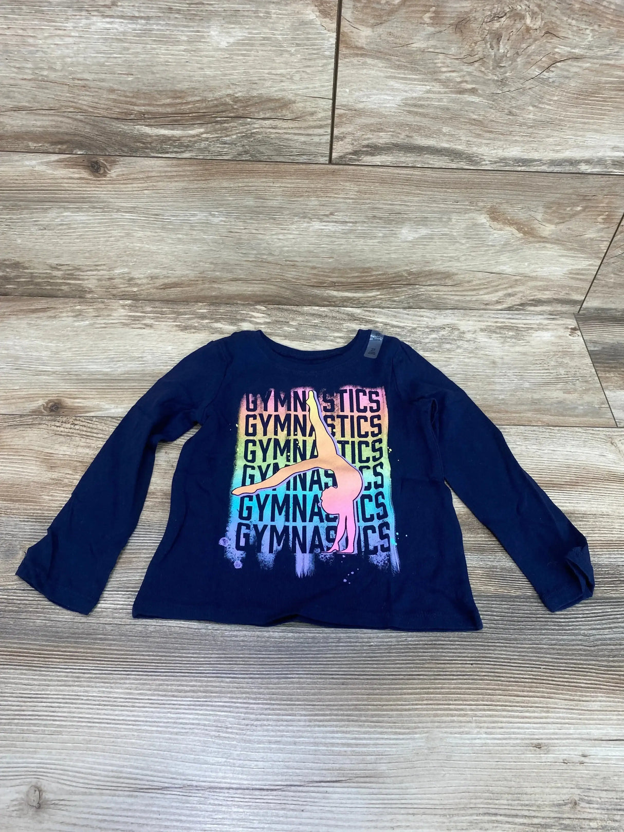 Front view of Children's Place navy long-sleeve toddler (2T) gymnastics shirt showing rainbow GYMNASTICS print and pink gymnast on wood floor