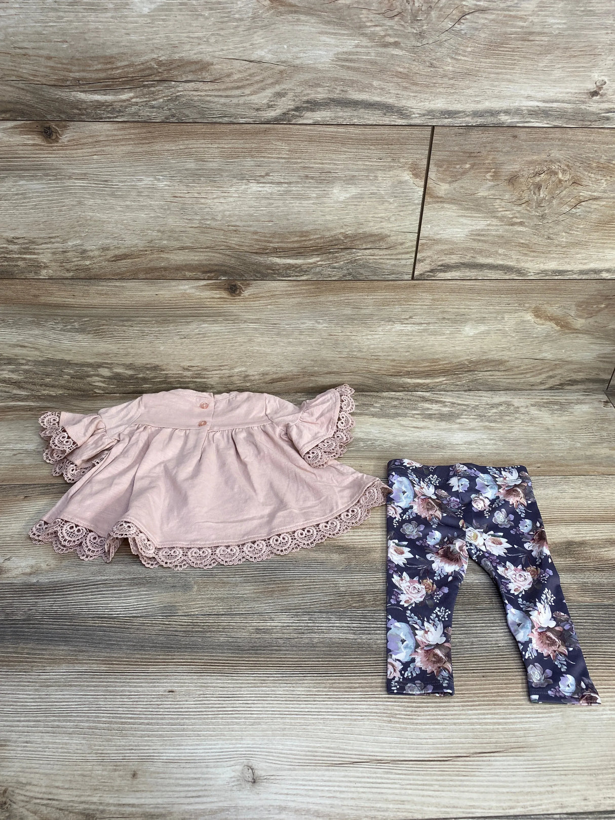 Top-down view of Cynthia Rowley 2-piece baby set: pink lace-trim top and navy floral leggings on wood background