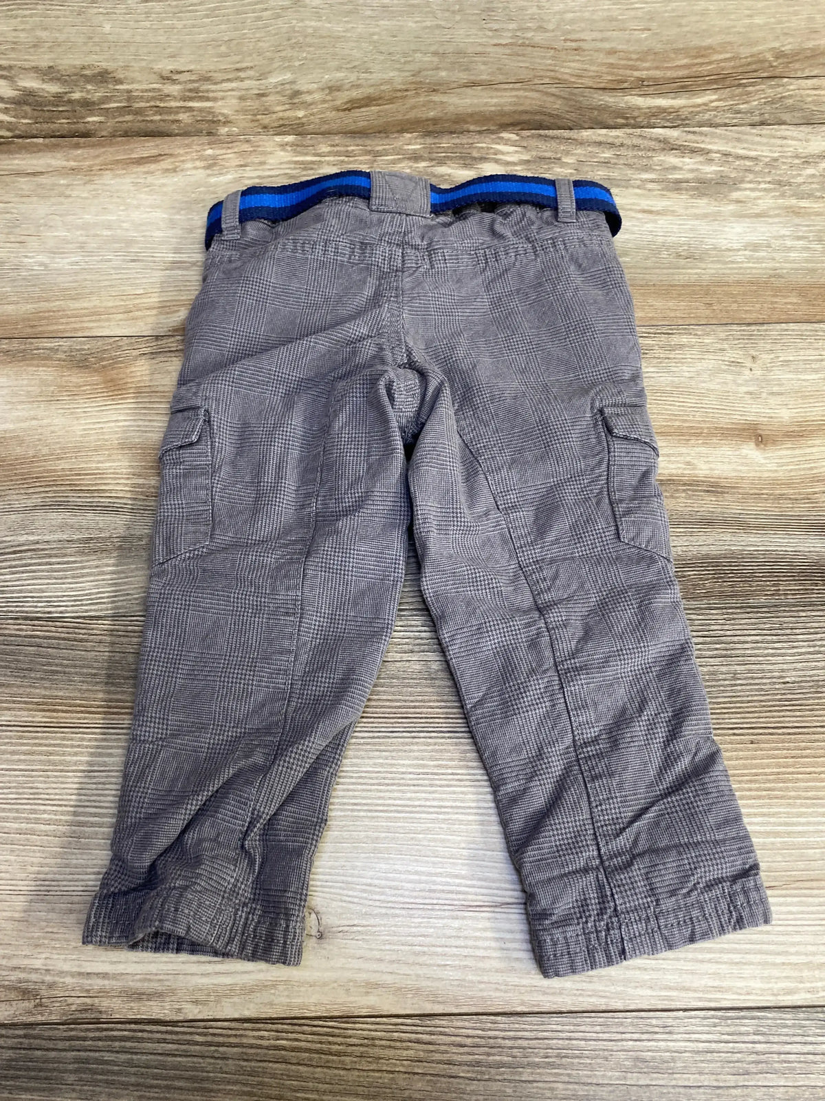Back view flat lay of H&M grey lined toddler pants with elastic waistband, blue striped belt, cargo pockets on wood