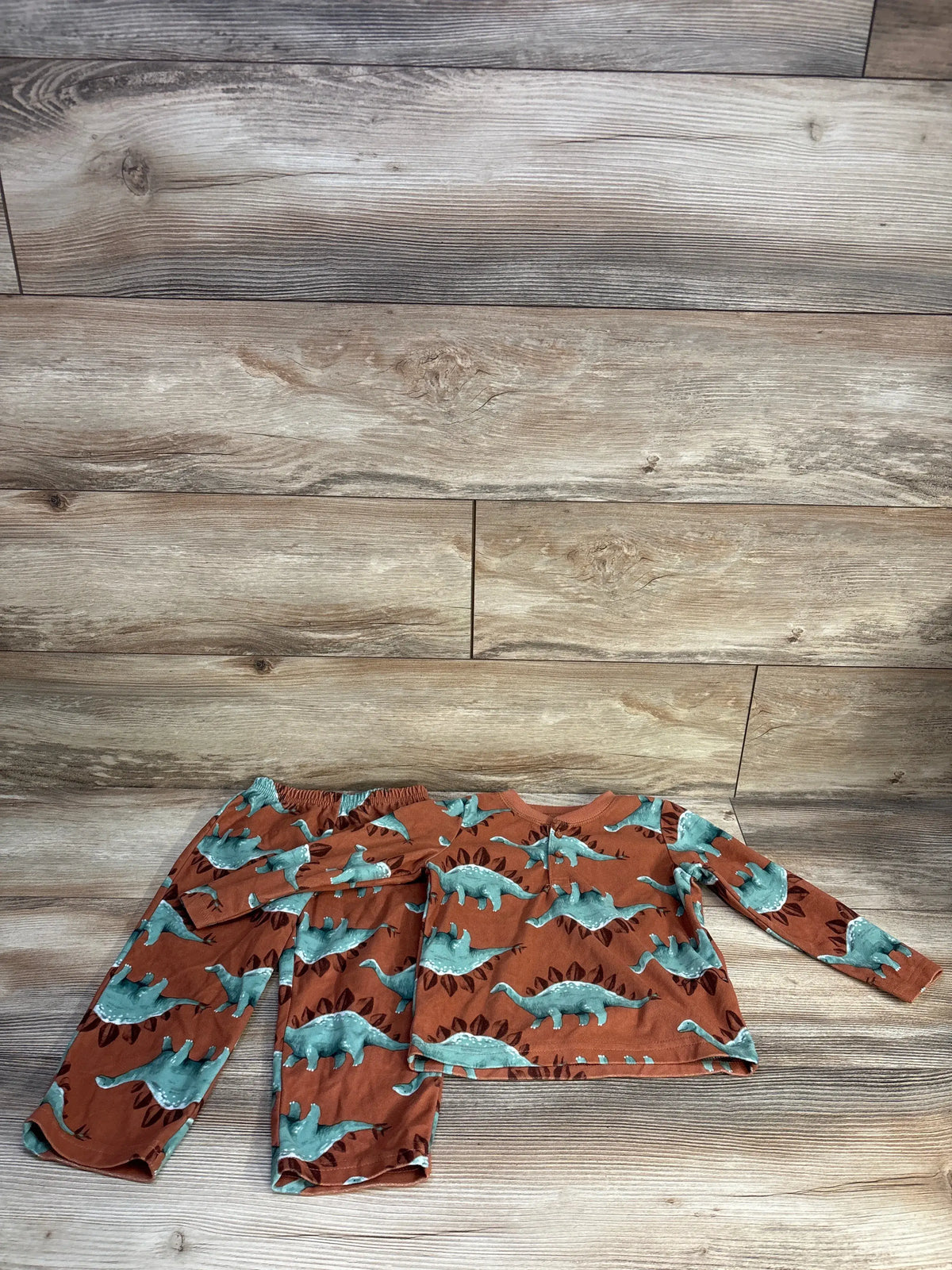 Flat lay of Just One You 2T dinosaur henley pajama set with brown fabric, teal dinosaur print, top and pants