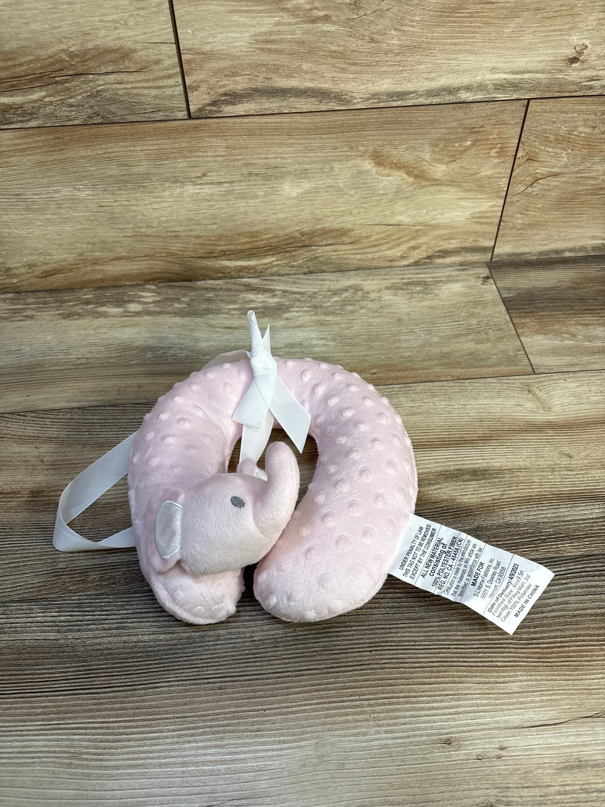 Top-down angled view of pink elephant U-shaped baby neck pillow showing textured minky dots and attached elephant head on wood background
