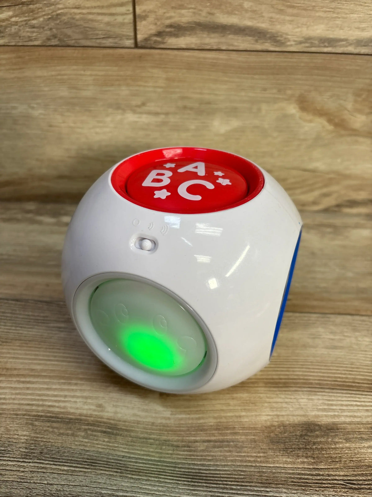 Front view of Best Learning Learning Cube showcasing illuminated green activity panel and ABC button on a wood floor