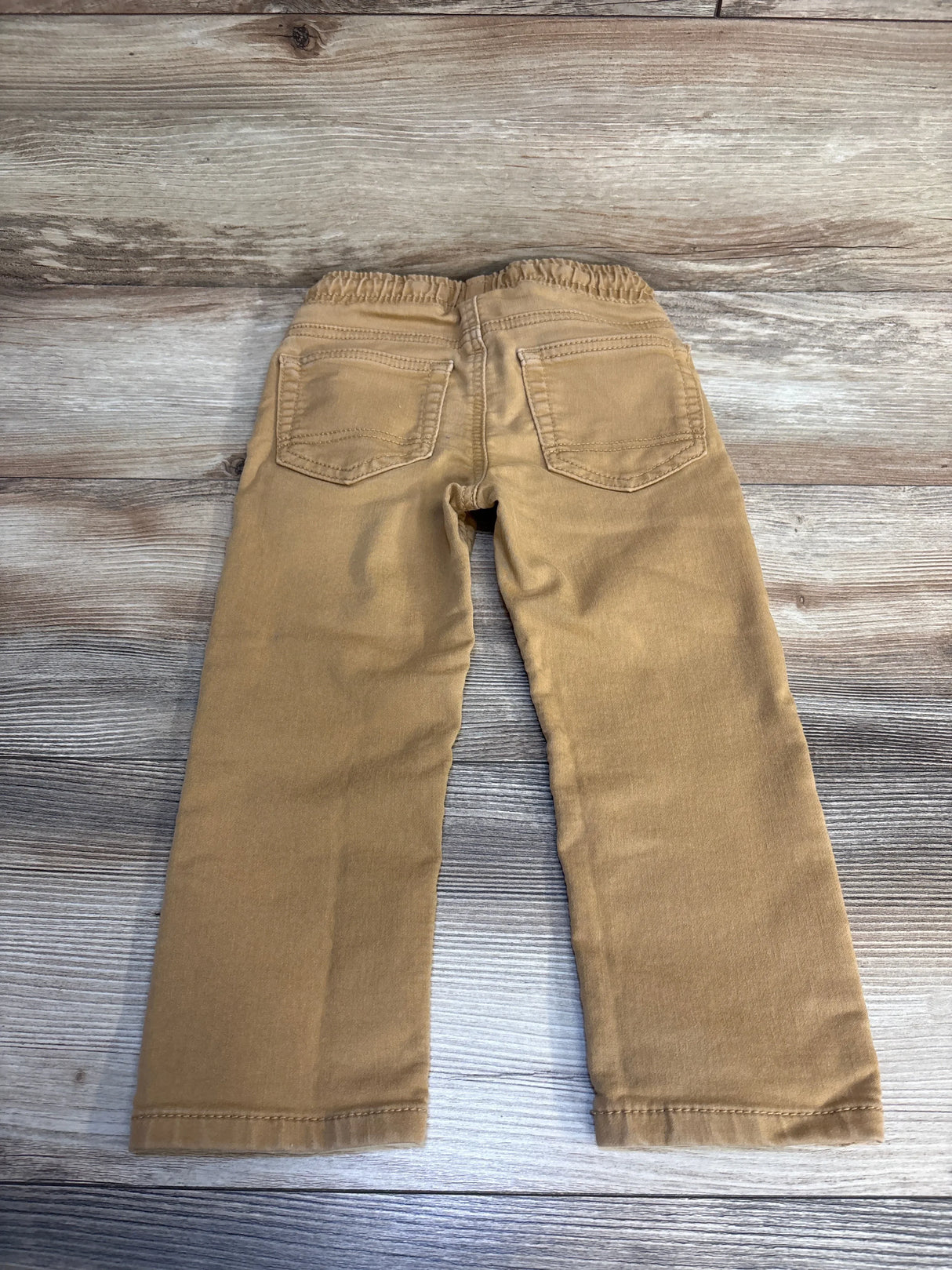 Tan toddler pants with elastic waist and back pockets on wood floor
