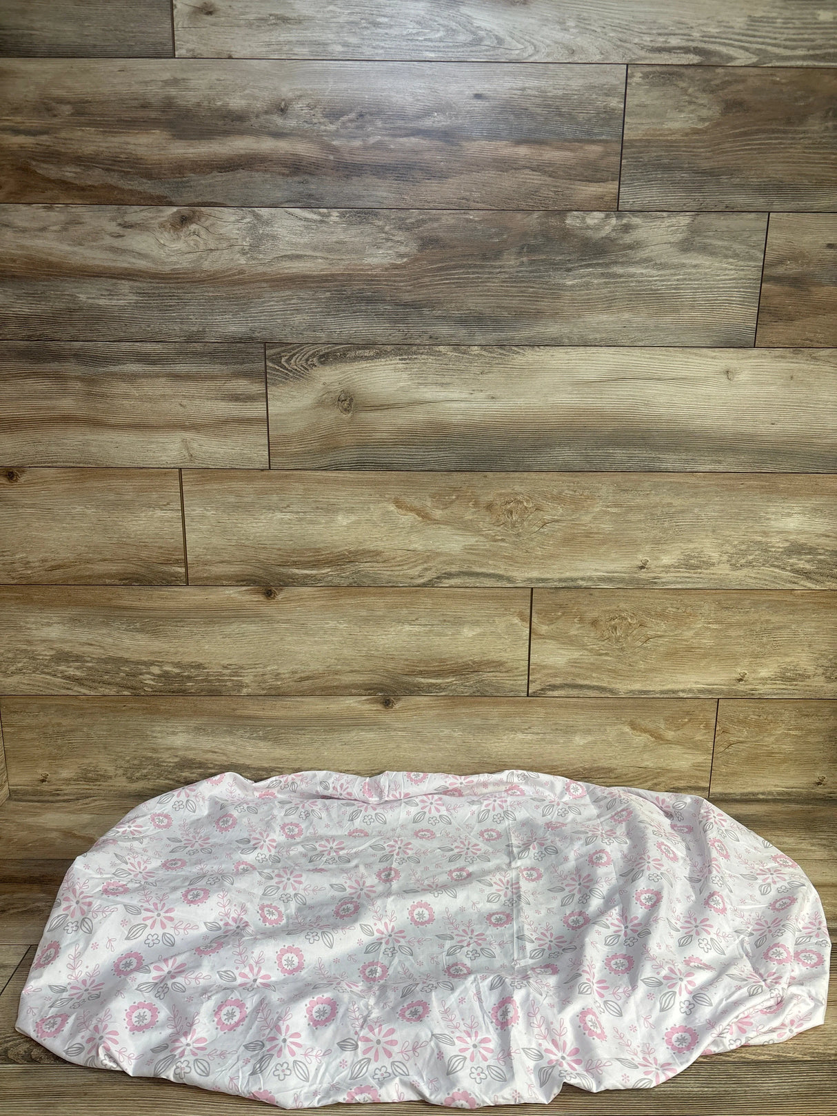 Top-down view of Peanutshell fitted crib sheet in white with pink and gray floral print showing elasticized fitted edge on wood-plank background