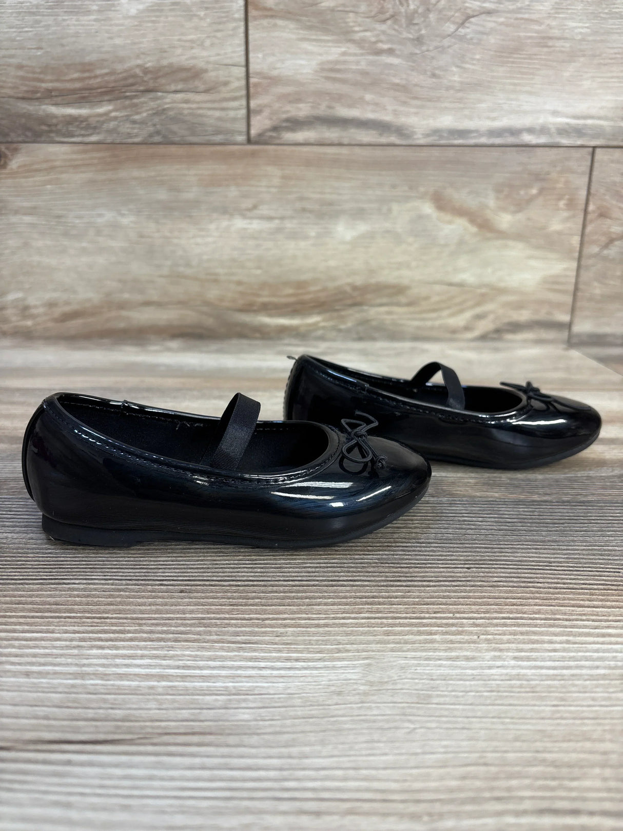 Black patent leather girls Mary Jane shoes with bow detail on wood floor