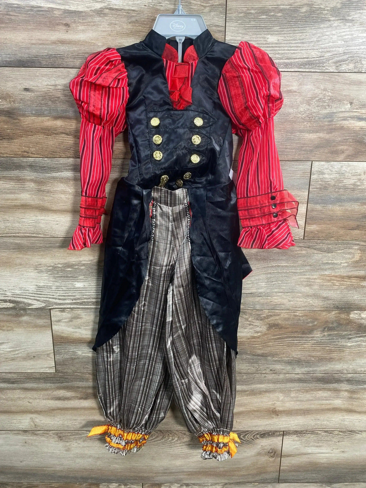 Front view of Disney Alice costume with black coat, gold buttons, red puff sleeves, and striped pants on wood background