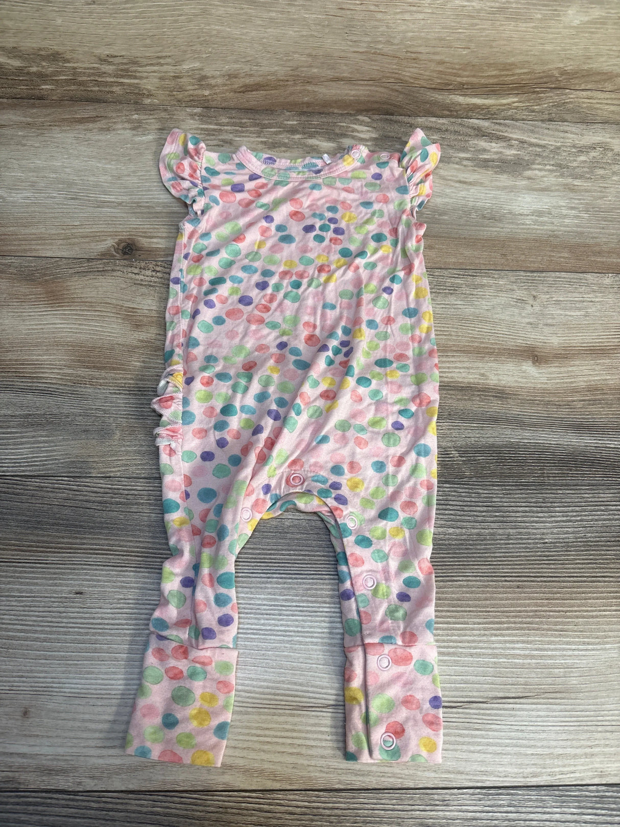 Colorful polka dot baby romper with ruffled sleeves on wood background