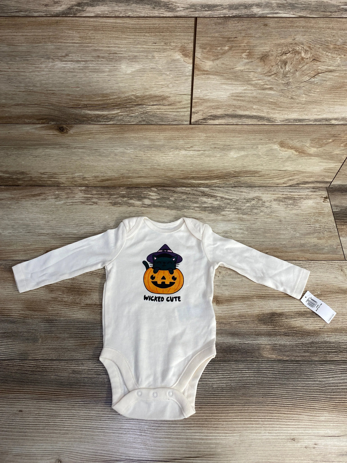White baby onesie with Halloween pumpkin and cat design, labeled 'Wicked Cute' on wood floor.
