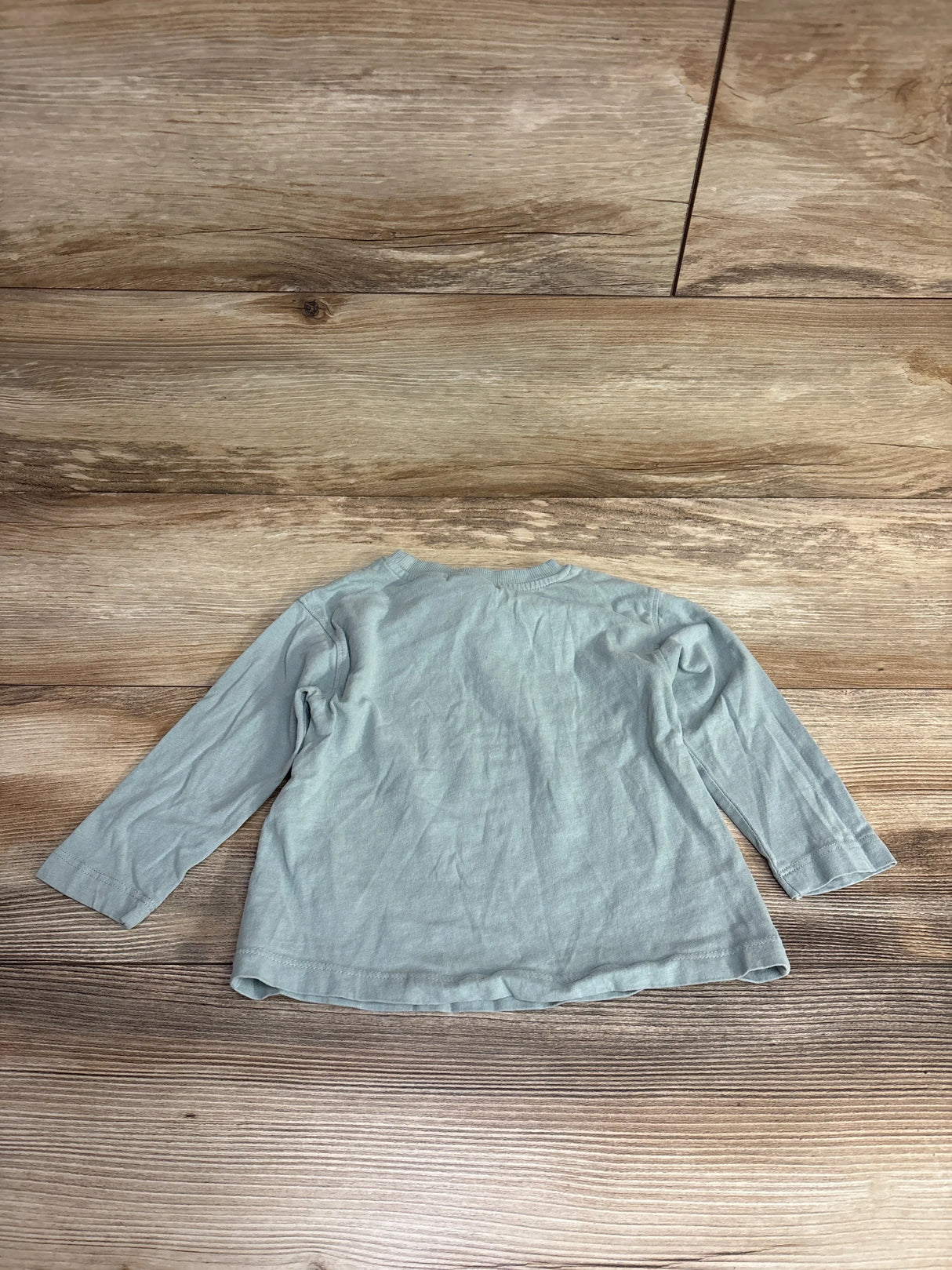 Light blue long-sleeve toddler shirt laid flat on wood floor in children's resale store