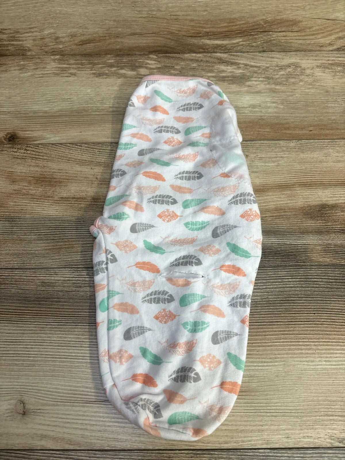 White baby swaddle blanket with pastel feather pattern on wooden surface