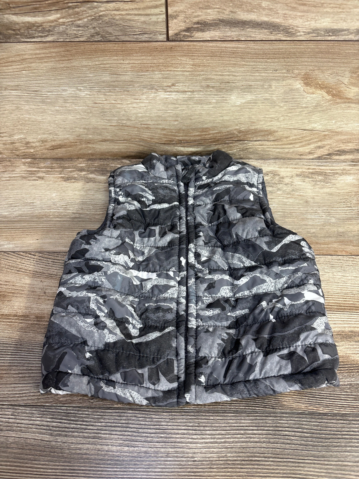 Gray and black camouflage padded sleeveless vest on wooden floor