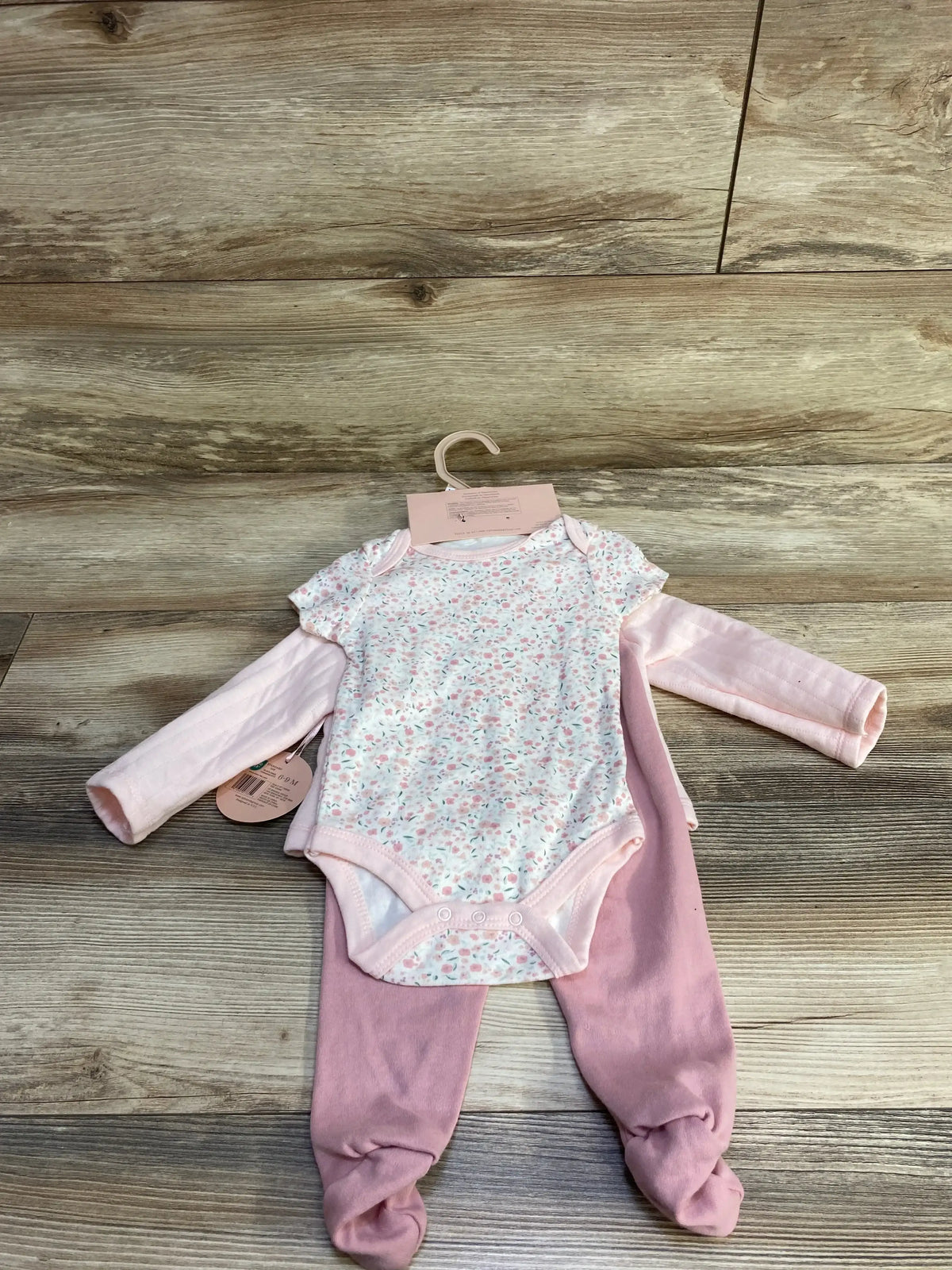 Flat lay of 4-piece pink baby set showing floral bodysuit layered over long-sleeve pink top and footed pants on wood