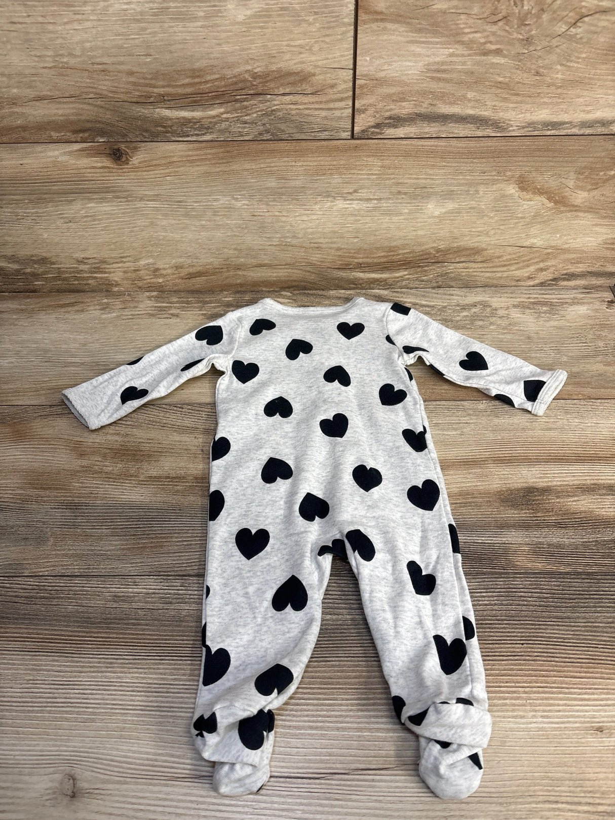 Gray baby onesie with black heart prints laid flat on wooden floor