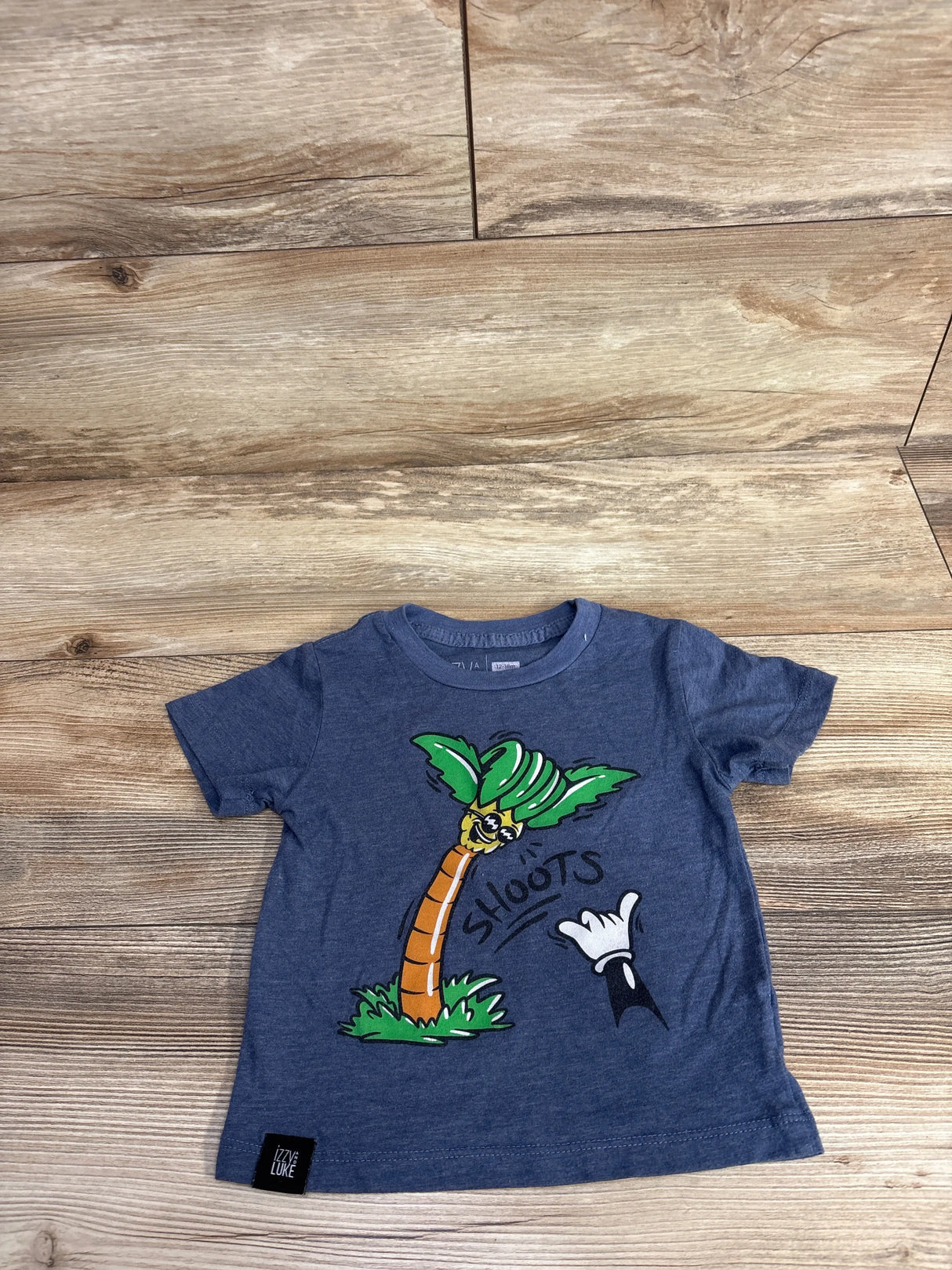 Blue toddler t-shirt with cartoon palm tree and 'Shoots' graphic on wooden background