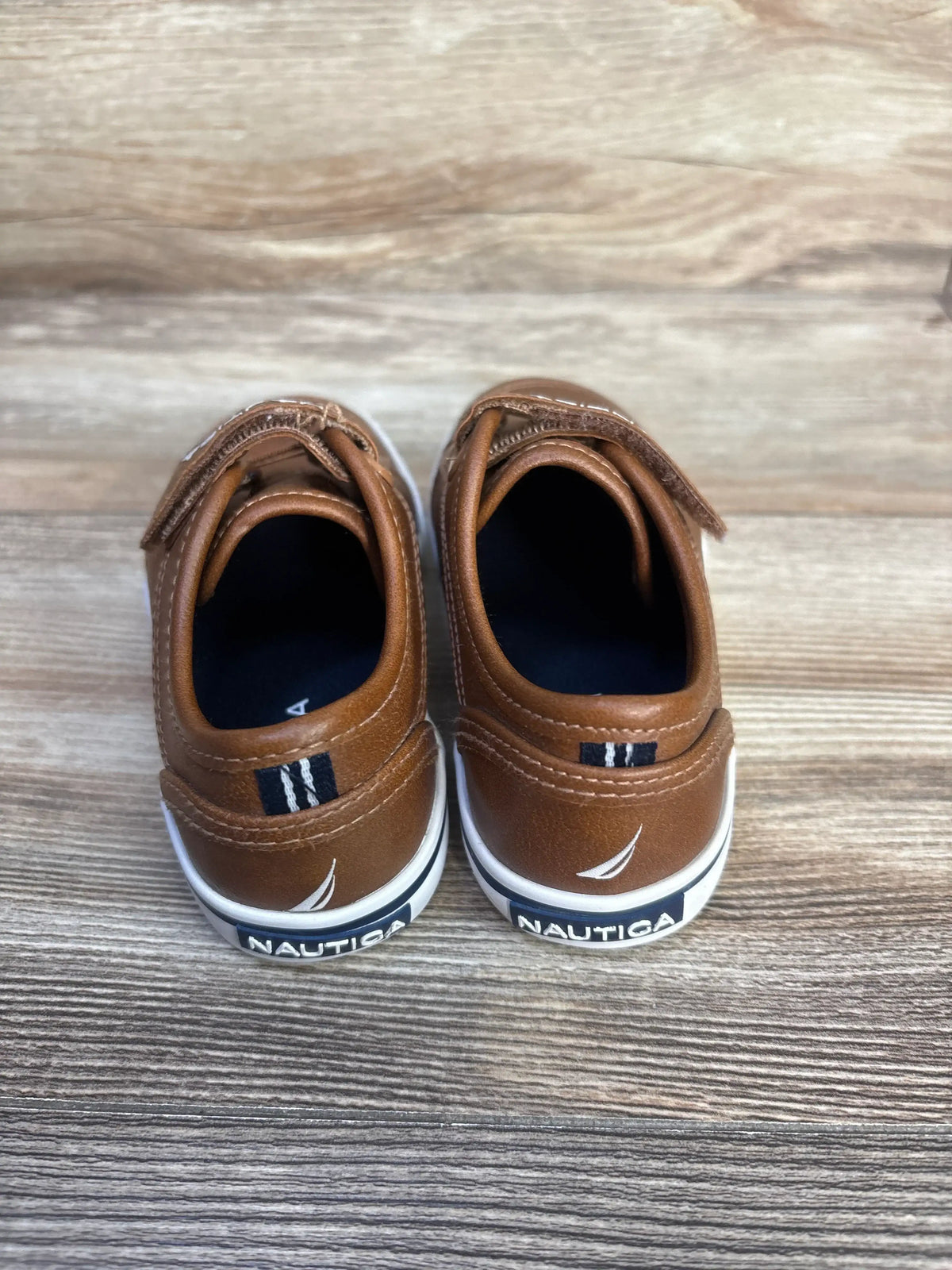 Rear view of Nautica Calloway brown faux leather sneakers, size 10C, showcasing white soles and Nautica branding on wood grain