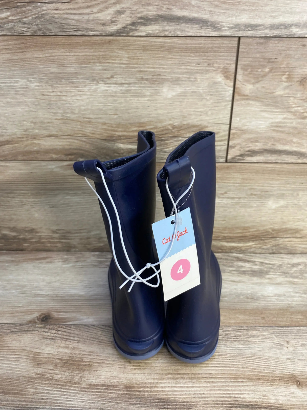 Rear view of navy Cat and Jack Andy slip-on children’s rain boots showcasing pull tabs and attached size tag with wood plank background