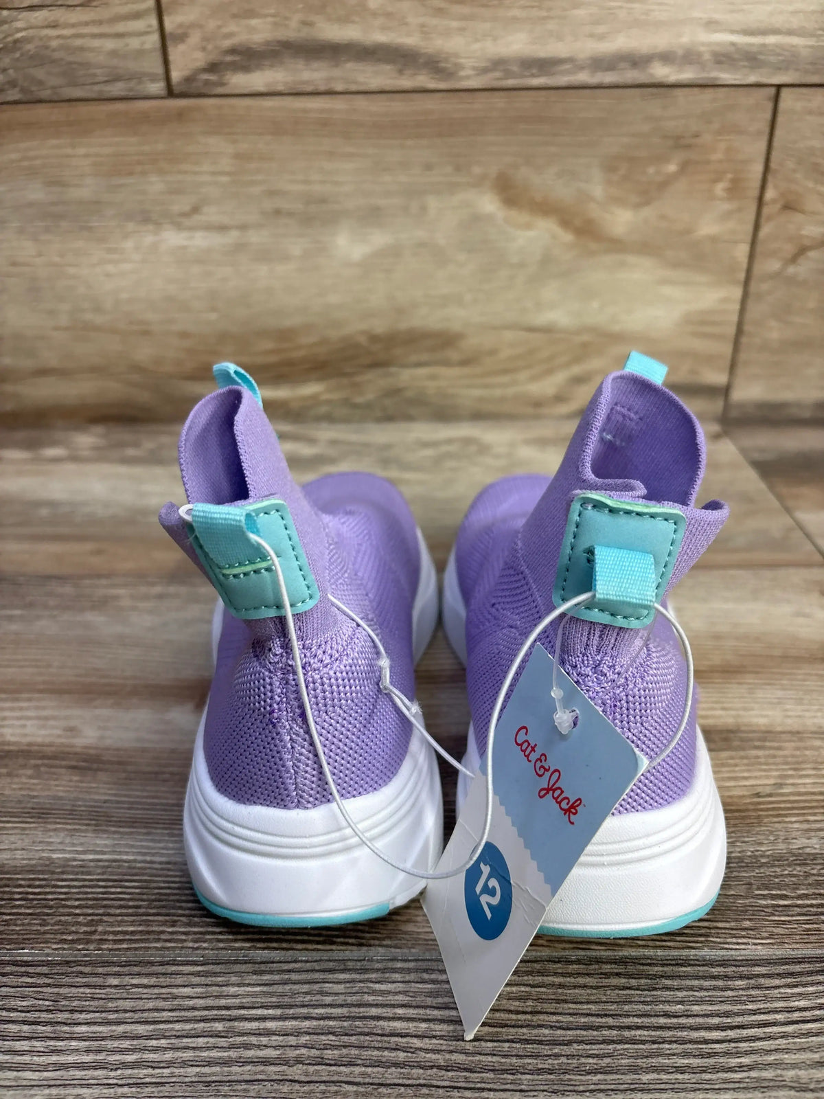 Rear view of Cat & Jack Ari toddler sneakers, purple knit, teal heel tabs, white soles, size 12 tag on wood floor