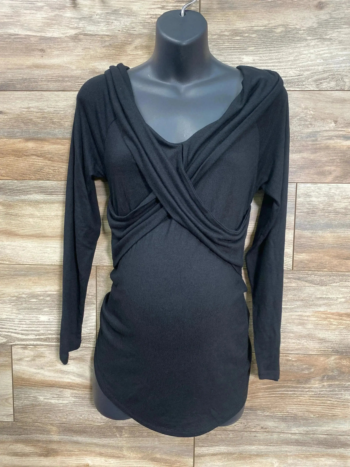 Front view of Isabel Maternity black long sleeve cross front top with draped neckline on black mannequin on wood plank floor