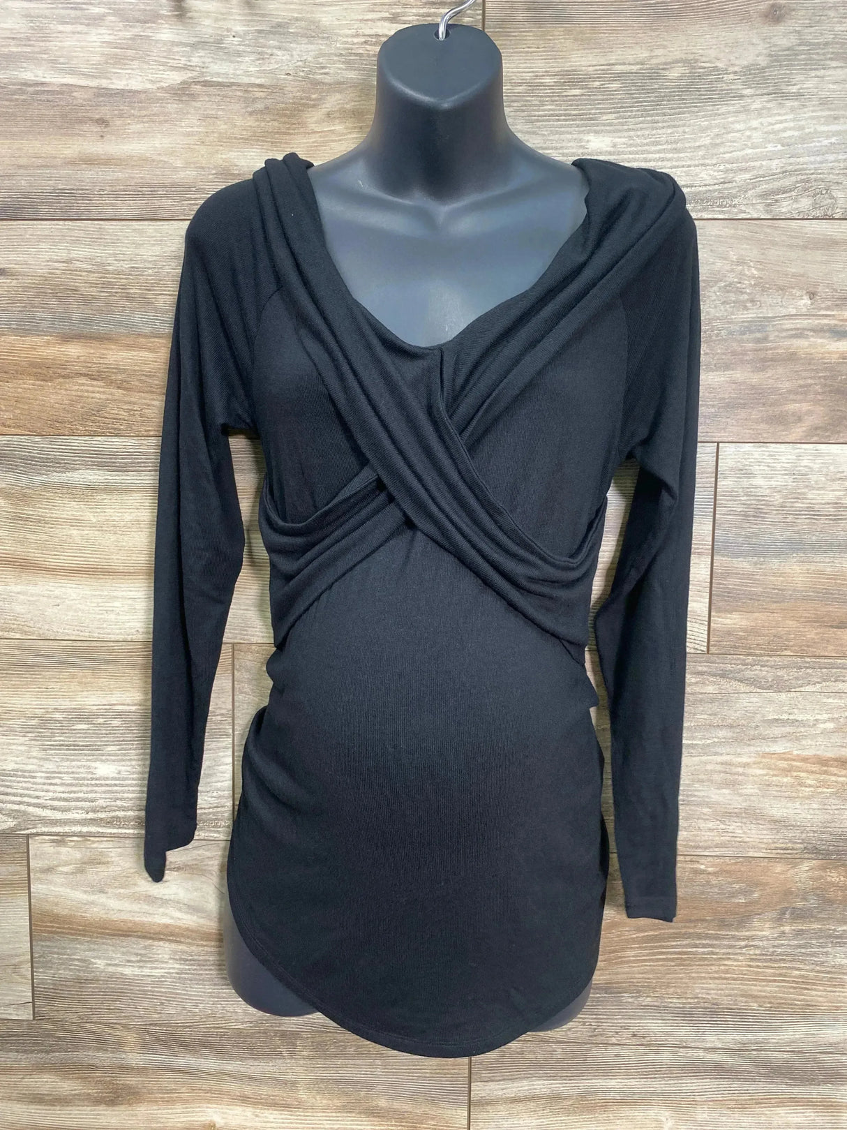 Front view of Isabel maternity top in black, cross-front wrap with ruched waist on mannequin against wood panel background