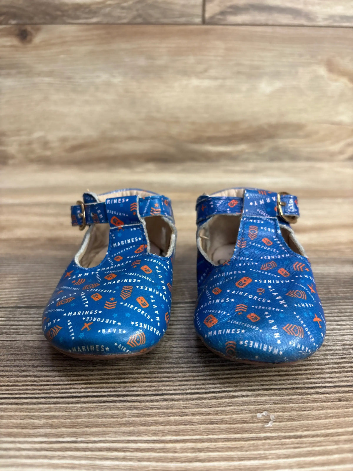 Front view of Monkey Feet T strap toddler shoes in blue with military branch print and ankle buckle on wooden floor