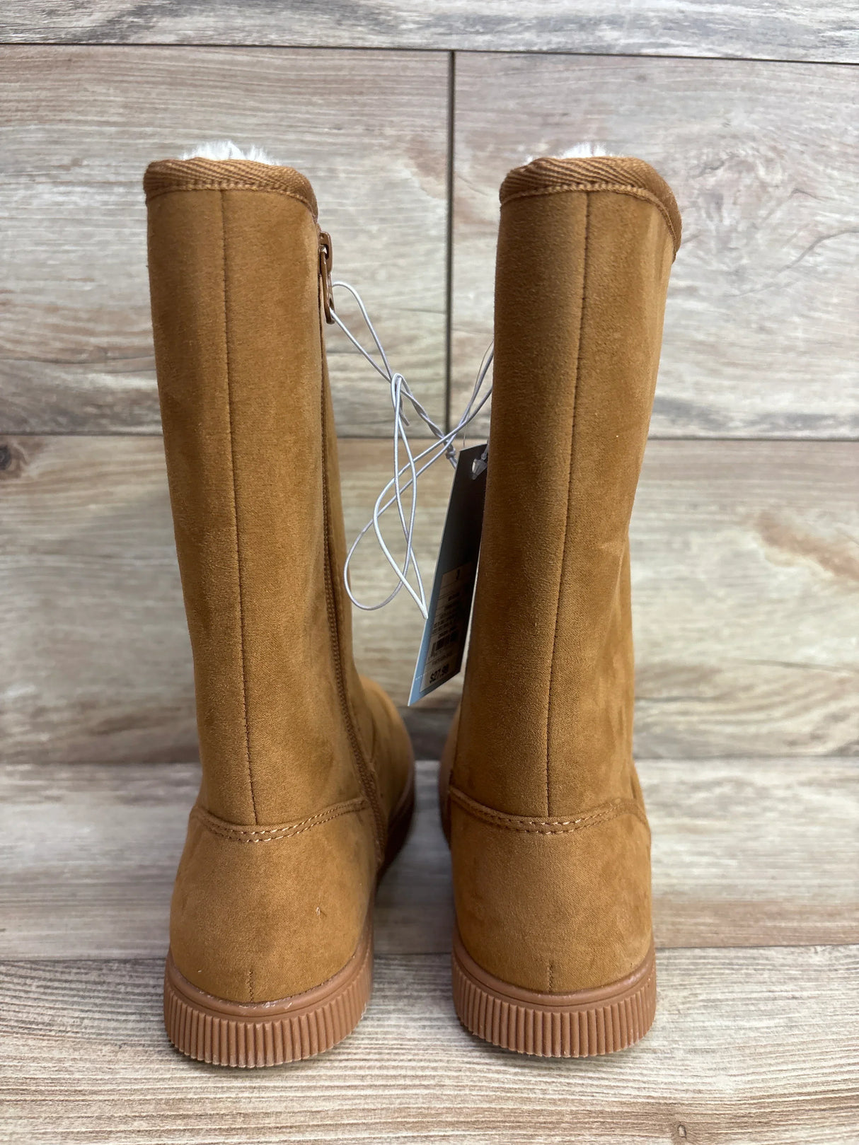 Back view of brown suede kids winter boots with rubber soles on wood floor