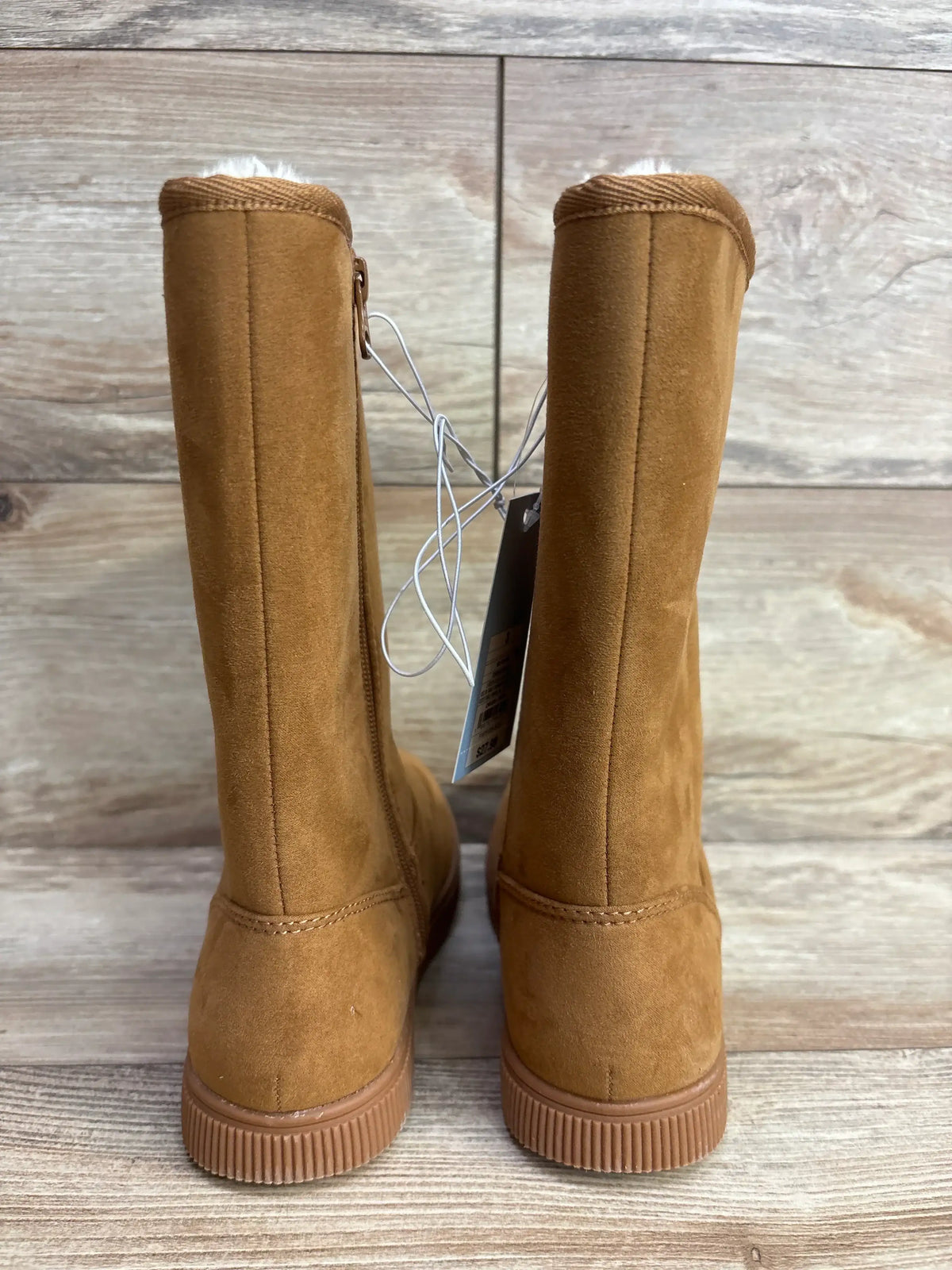 Back view of brown suede kids winter boots with rubber soles on wood floor