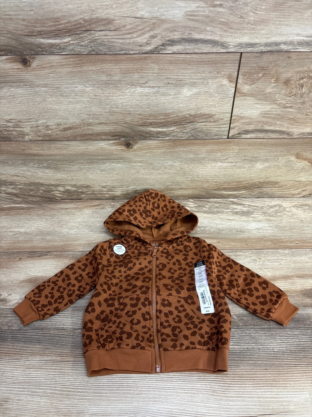 Brown leopard print baby hoodie with zipper and tags on wood background