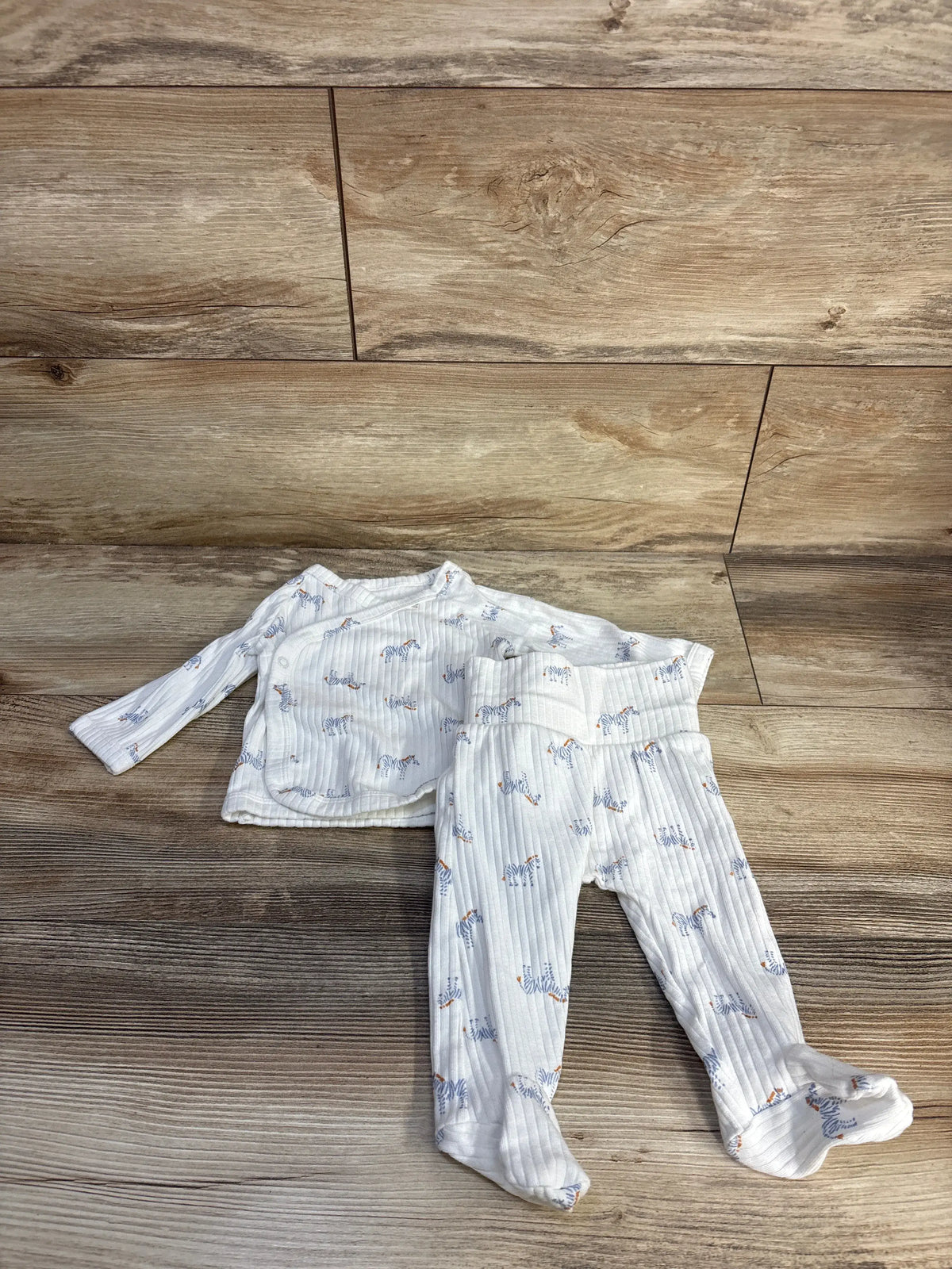 Top-down view of Just One You two-piece ribbed zebra kimono set showcasing white fabric and footed bottoms on a wood floor