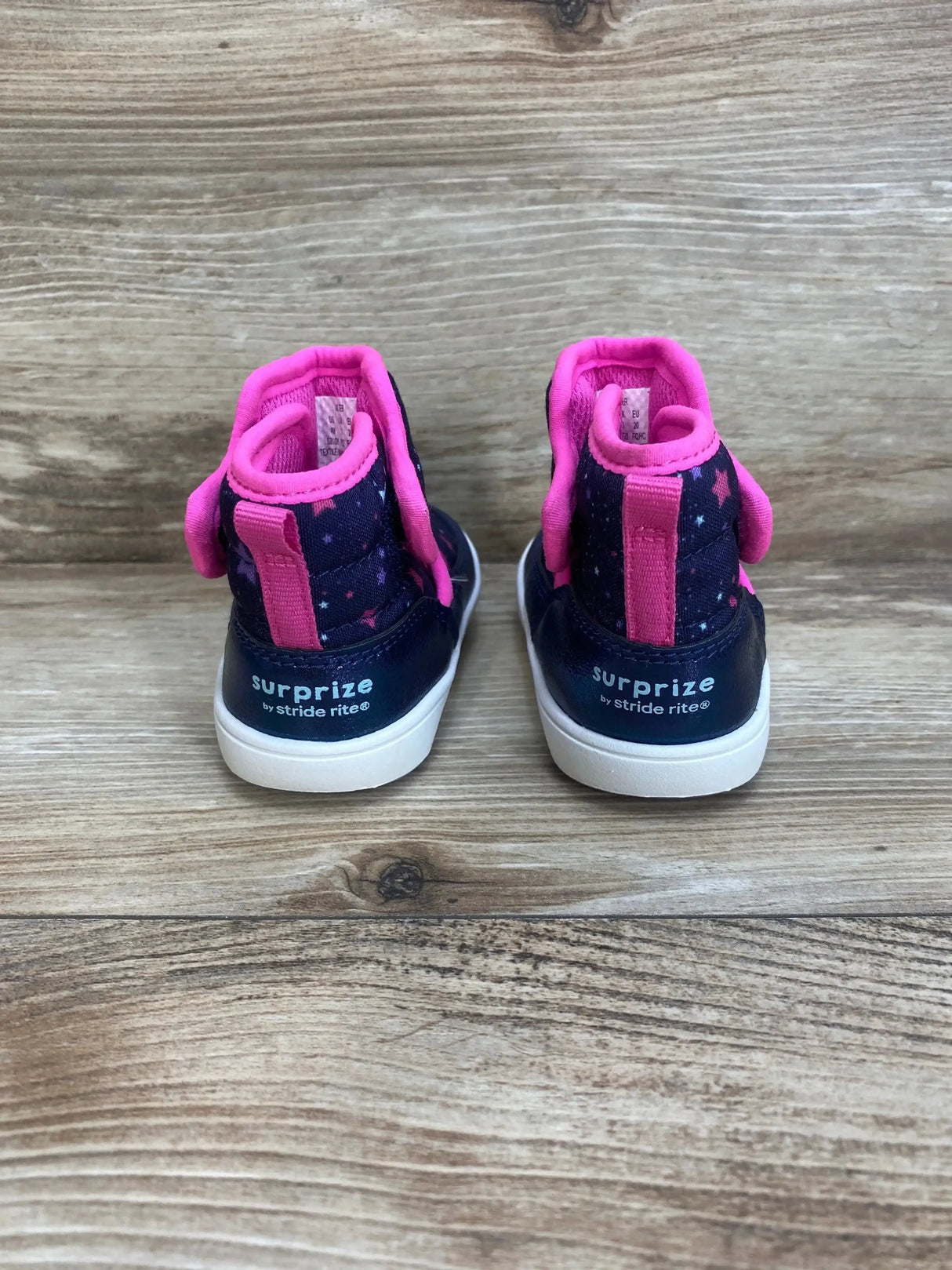 Rear view of Surprize by Stride Rite Aster toddler winter boots, navy with pink trim and star print, white soles on wood