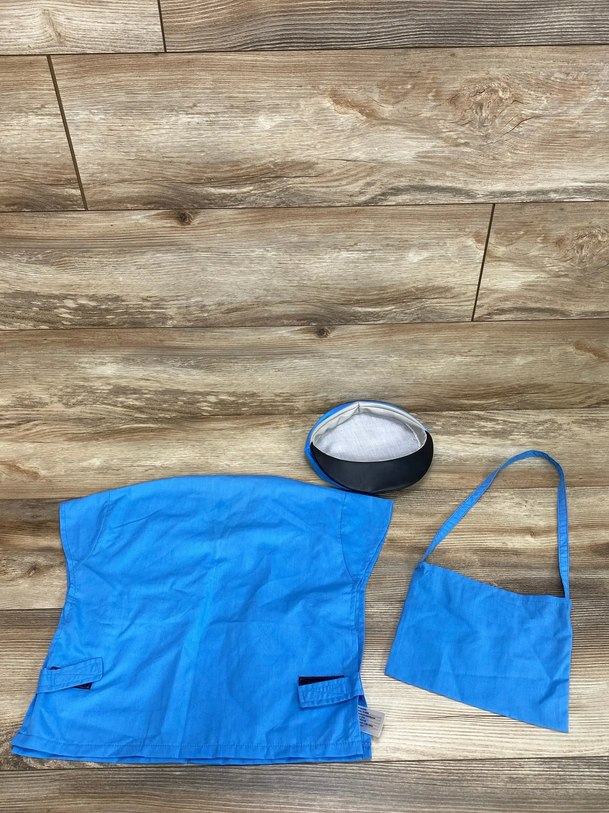 Overhead view of a blue toddler mail carrier costume showcasing a matching cap and shoulder bag with a wood floor background