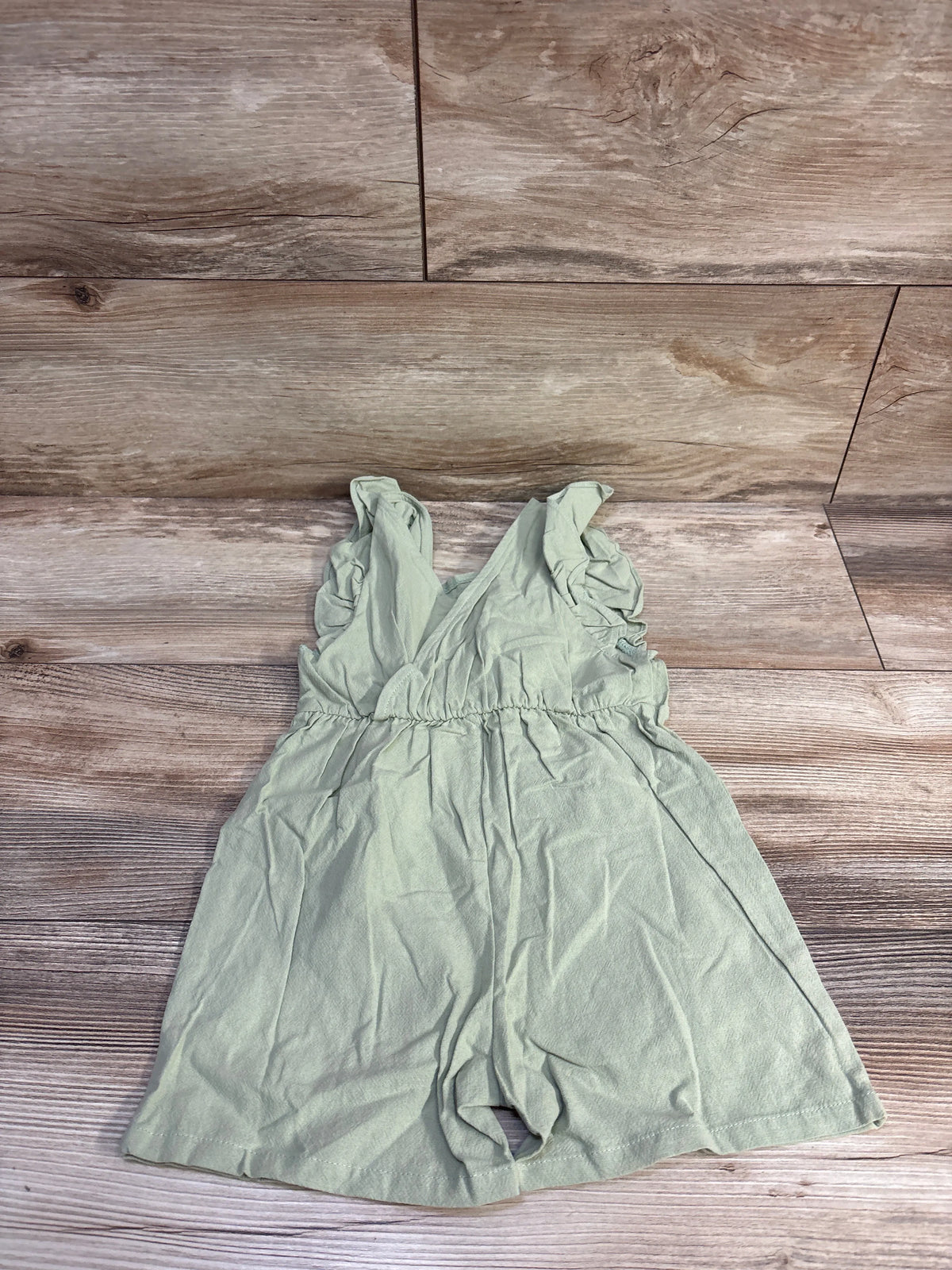 Flat lay of green flutter-sleeve shortie romper showing ruffled sleeves and gathered elastic waist on wood background