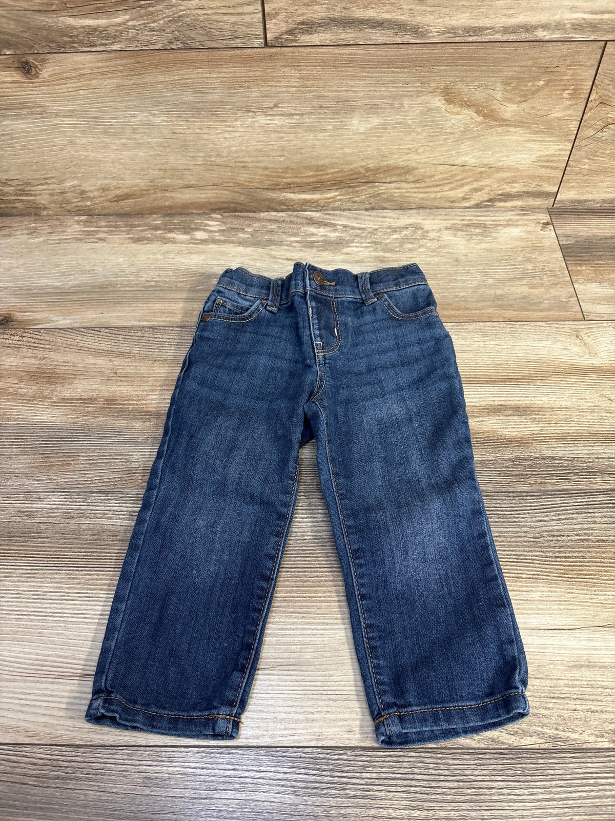 Front view of OshKosh baby jeans, size 18 months, showcasing front pockets and zip fly on a wood floor