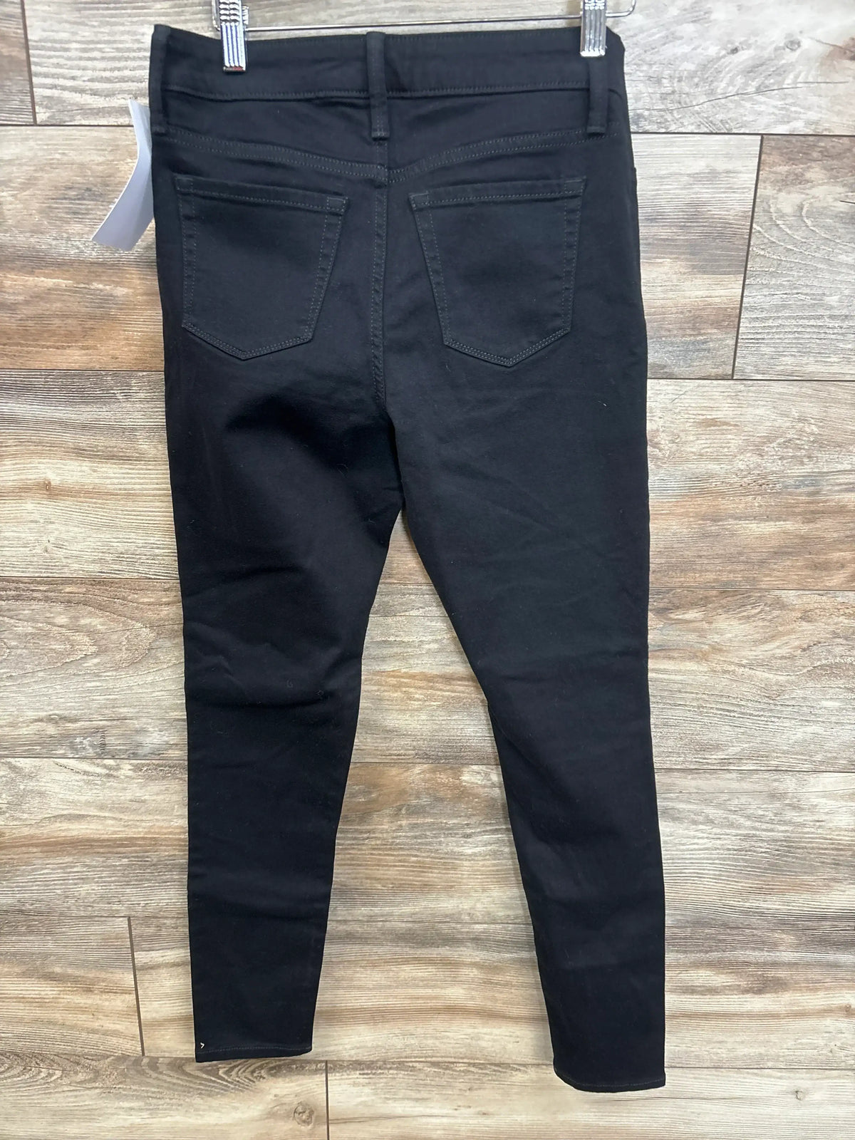 Back view of black Isabel maternity side-panel skinny jeans size XS showing back pockets and tapered legs against wood floor