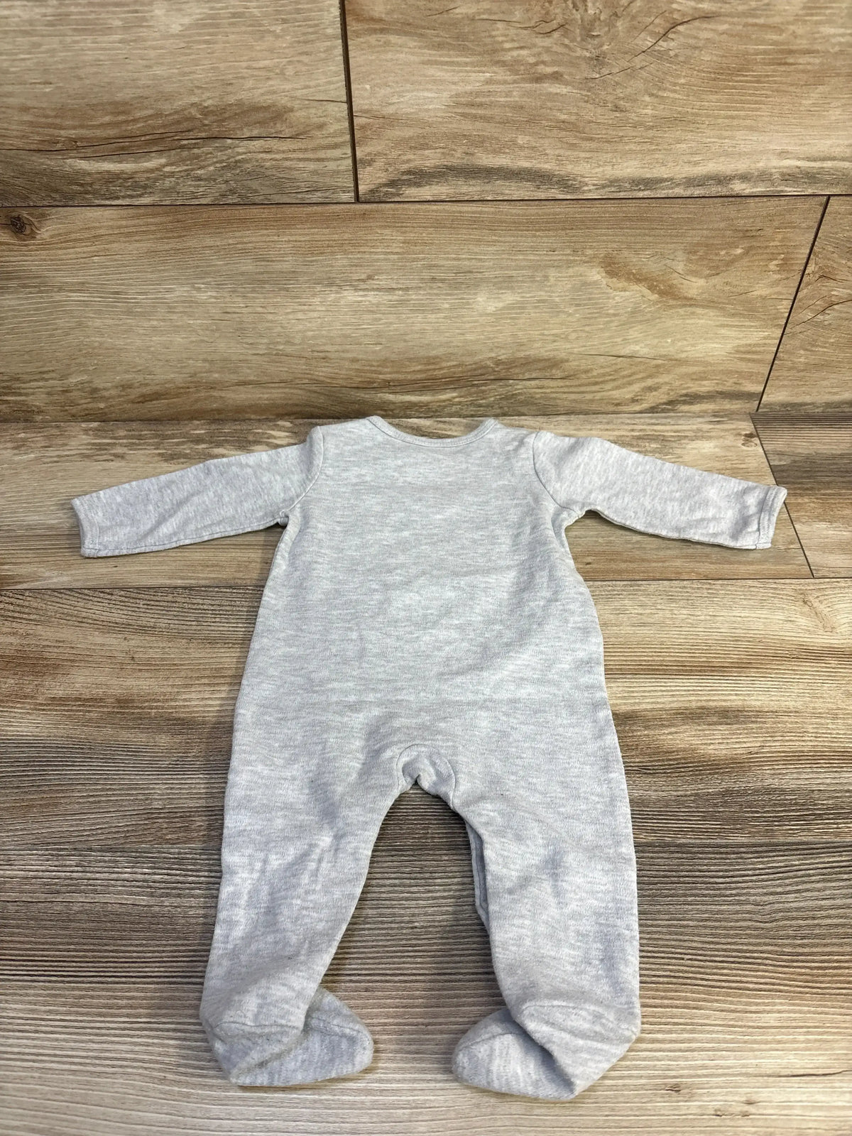 Back view of grey Hello Kitty footed coverall showing long sleeves, enclosed feet, and light heather fabric on wood floor background
