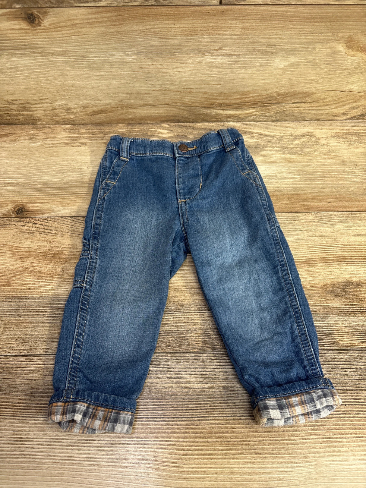 Toddler blue denim jeans with plaid cuff details on wooden background