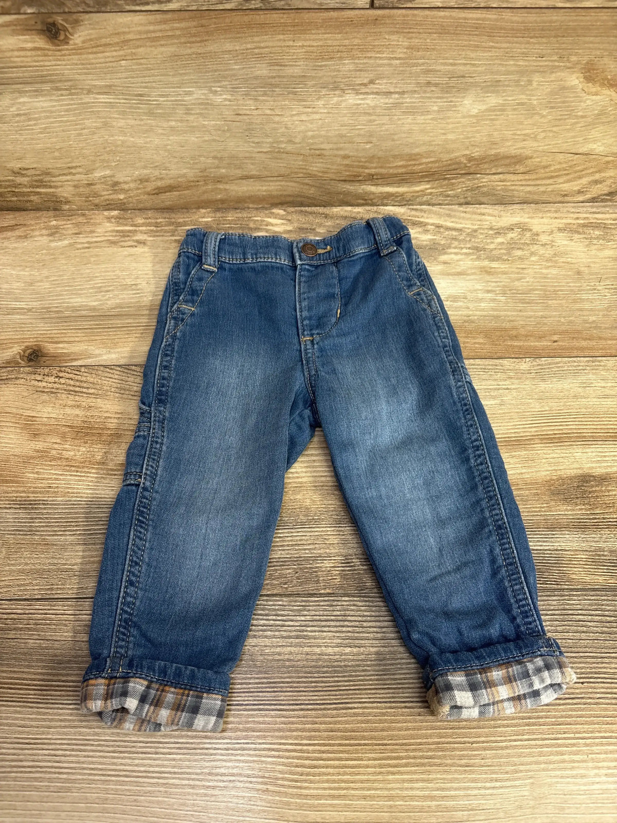 Toddler blue denim jeans with plaid cuff details on wooden background