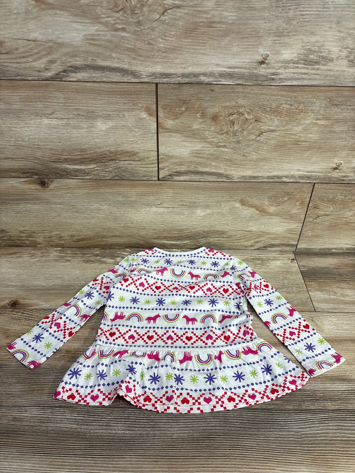 Children's long-sleeve white shirt with colorful unicorn, rainbow, heart, and snowflake patterns on wooden floor