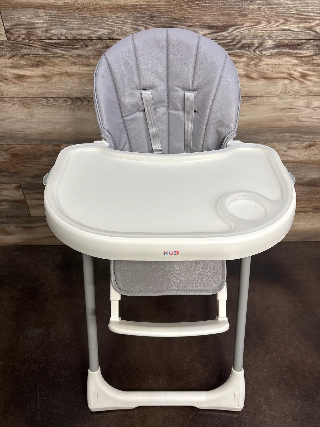 Front view of KÜB 3-in-1 high chair showcasing grey padded seat with harness and removable white tray on wood background
