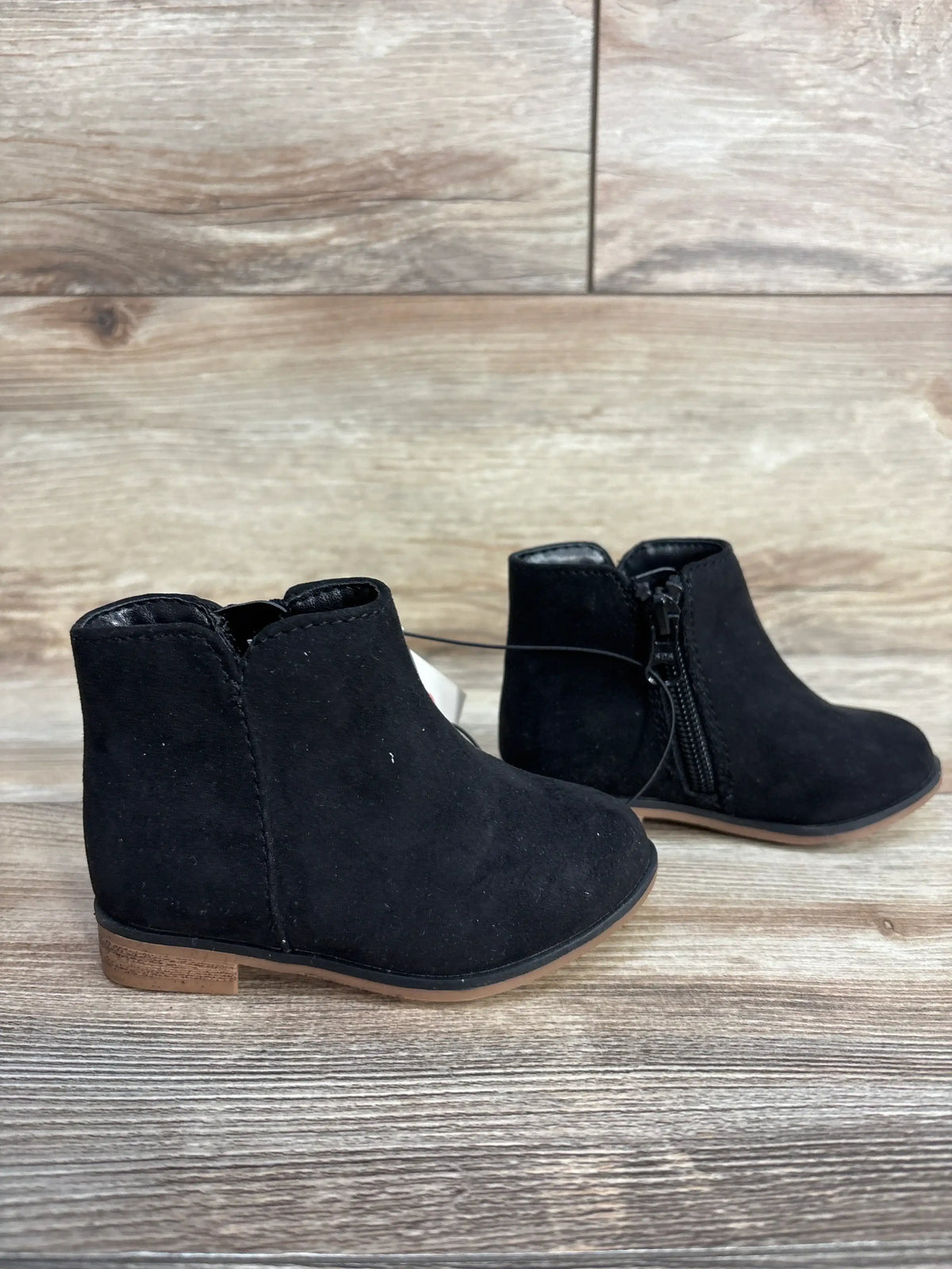Black suede ankle boots for kids with side zippers on wooden floor background