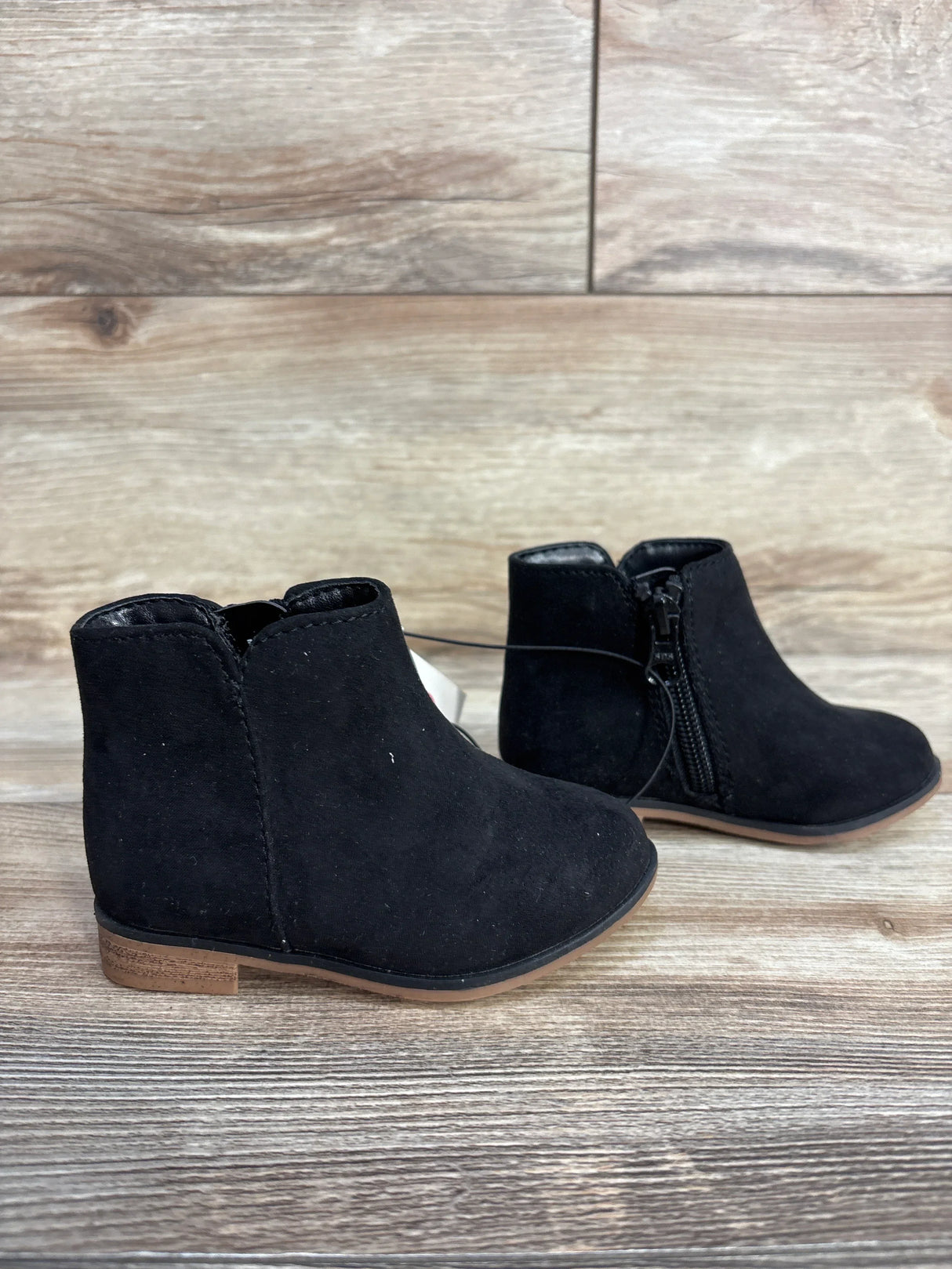 Black suede ankle boots for kids with side zippers on wooden floor background
