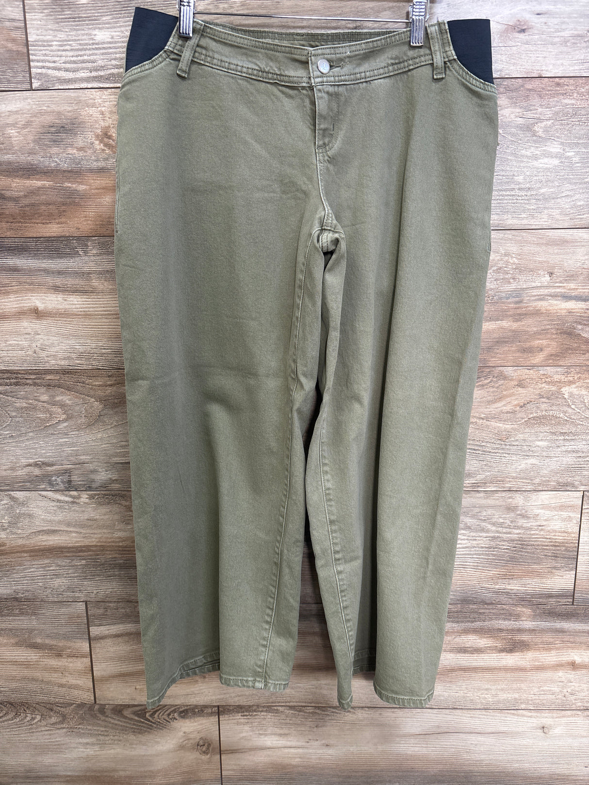 Front view of green Isabel maternity wide-leg jeans showing black side stretch maternity panels hanging on clips against wood background