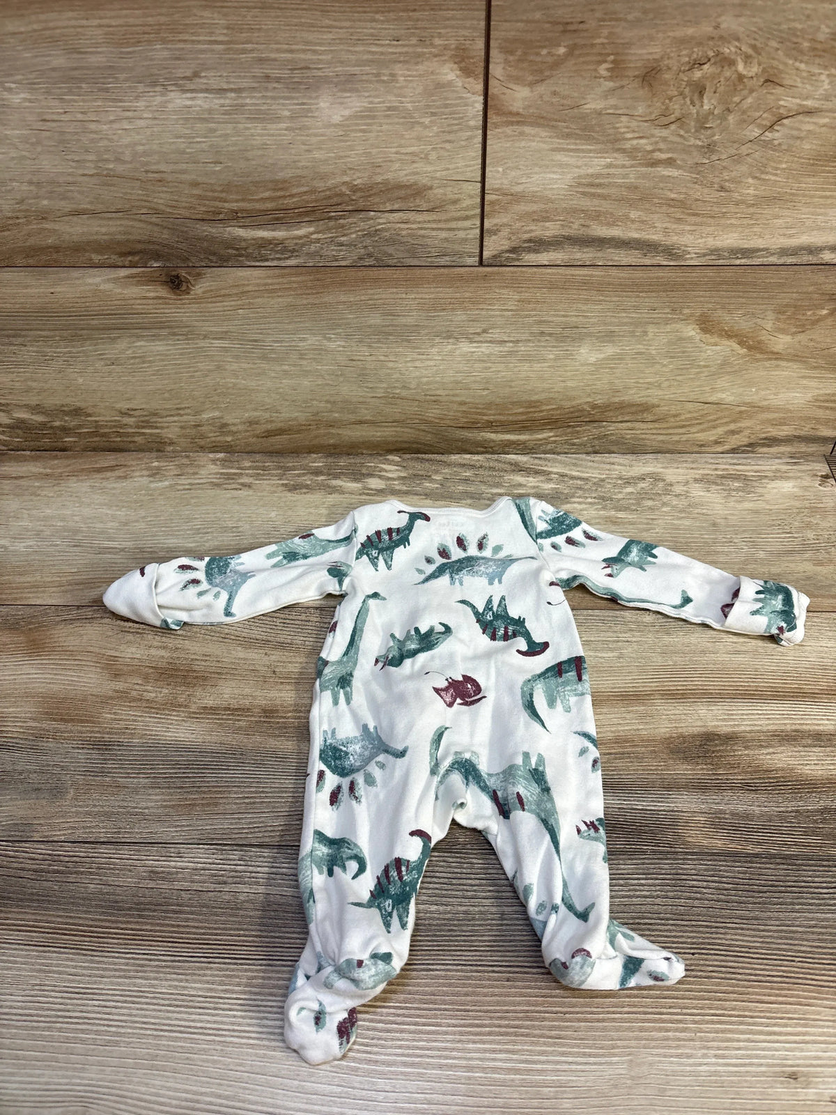 Back view of Just One You newborn white footed sleeper showing green and maroon dinosaur print on wood background