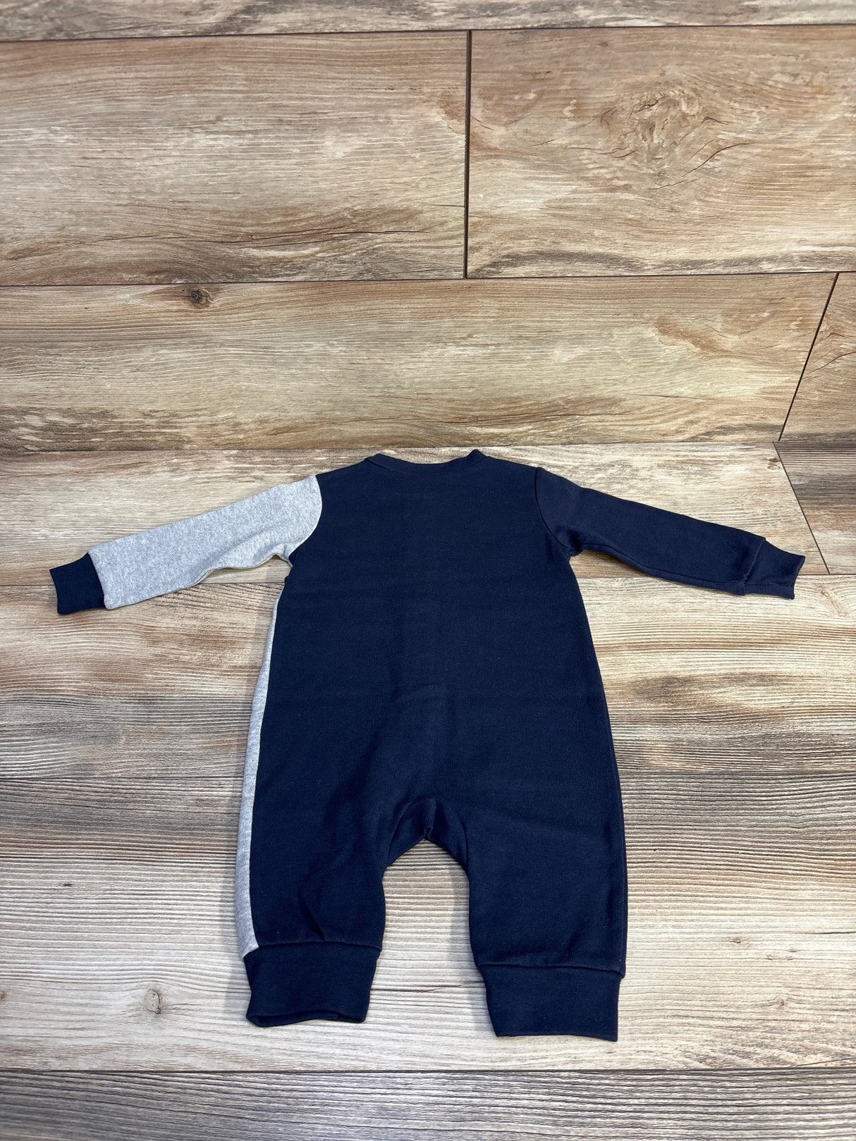 Back view of navy blue and gray long-sleeve baby romper on wooden floor