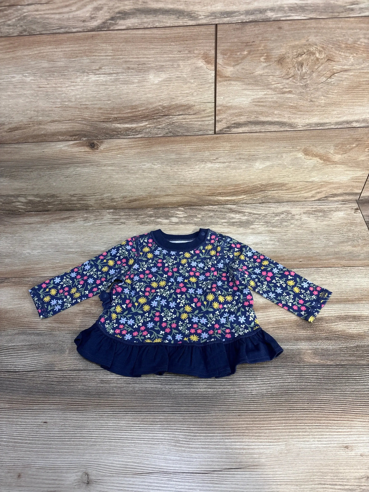 Navy blue baby dress with colorful floral print and ruffle hem on wood background