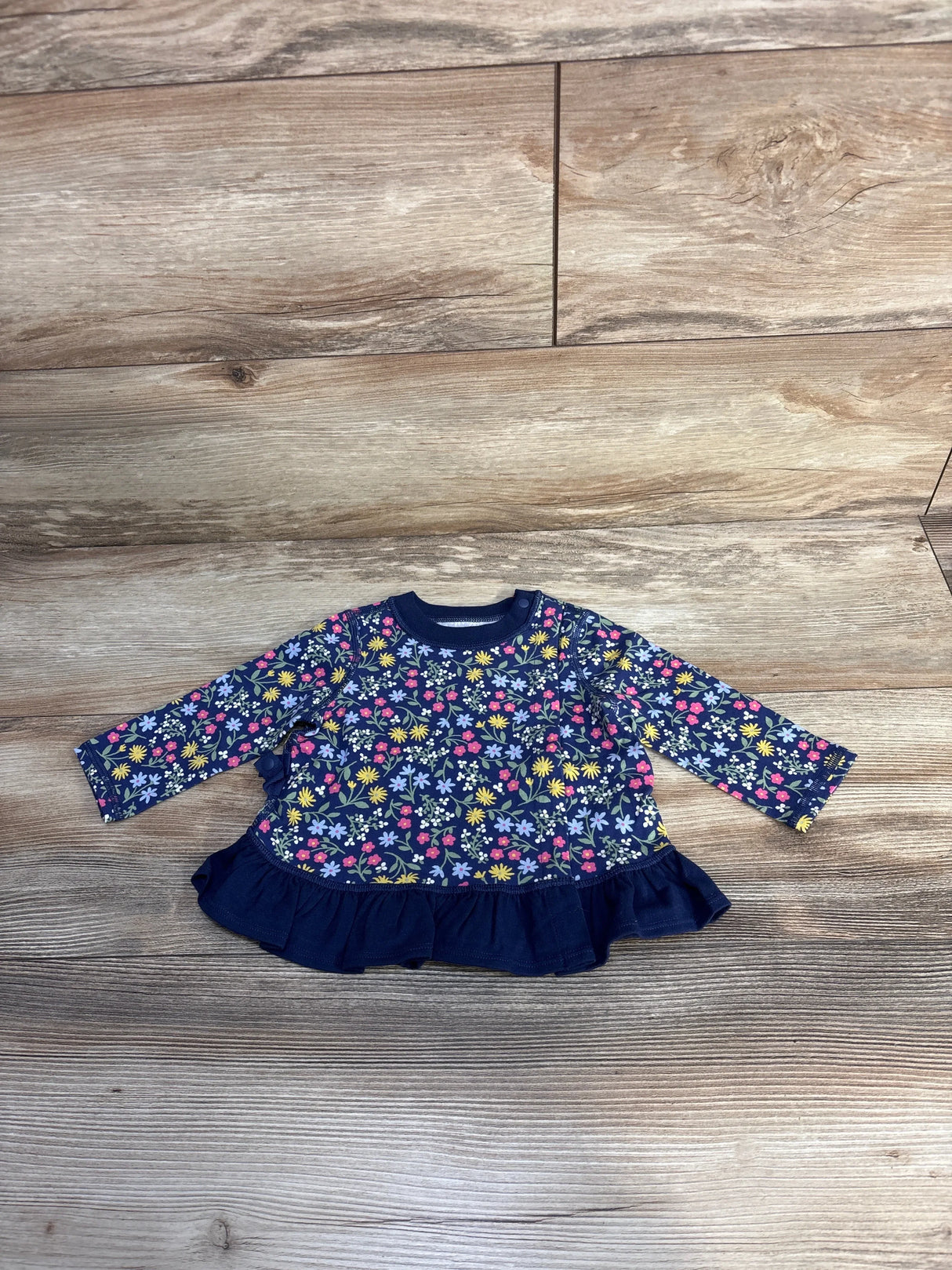 Navy blue baby dress with colorful floral print and ruffle hem on wood background