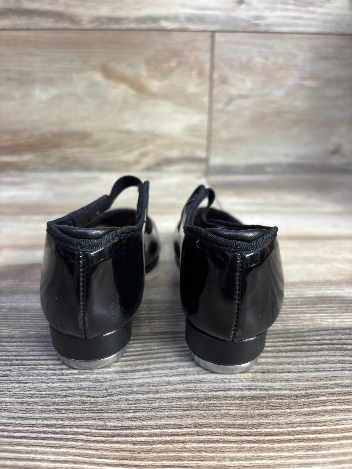 Black patent tap shoes rear view on wooden floor, children's dance footwear
