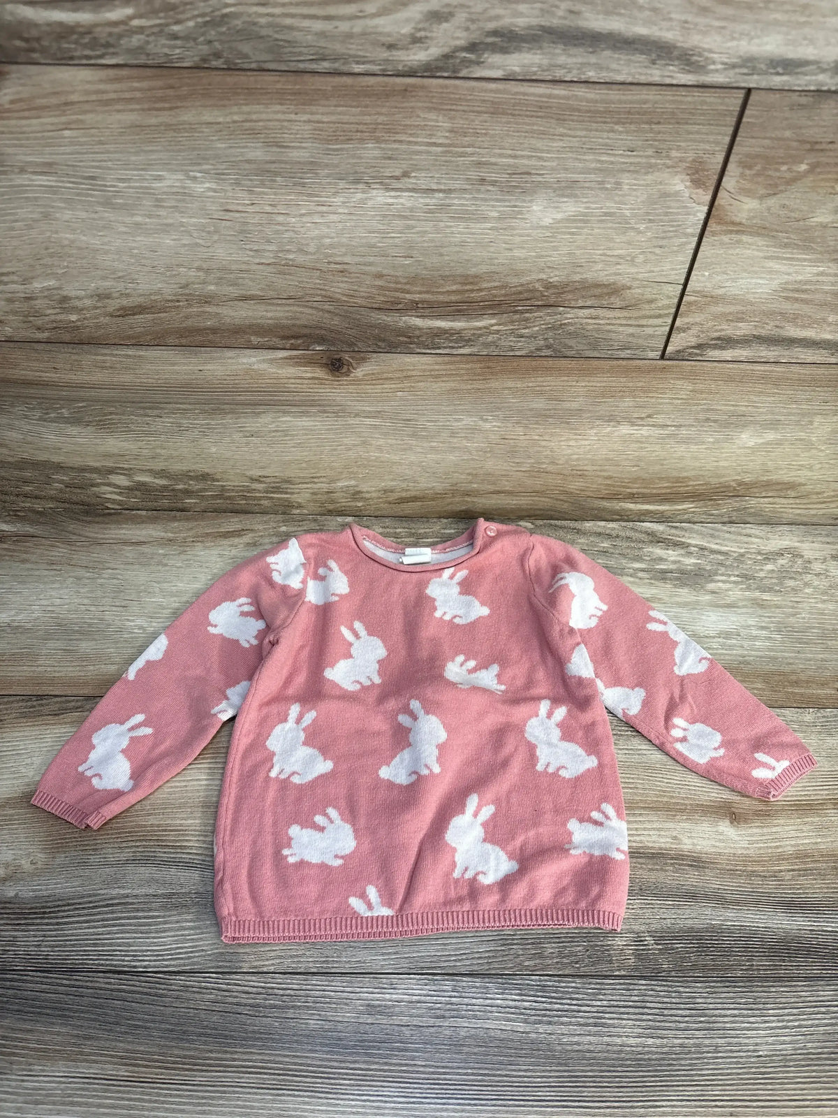 Pink baby sweater with white bunny print, long sleeves, laid on wood floor