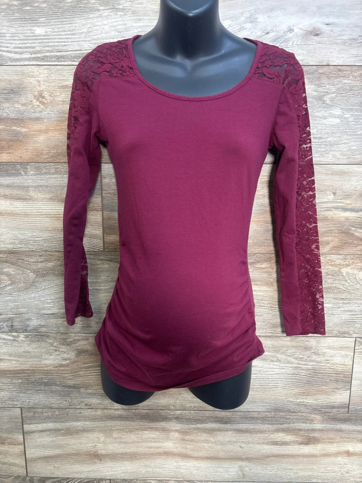 Front view of maroon Ambiance Maternity long sleeve top with lace sleeves and ruched sides on wood background