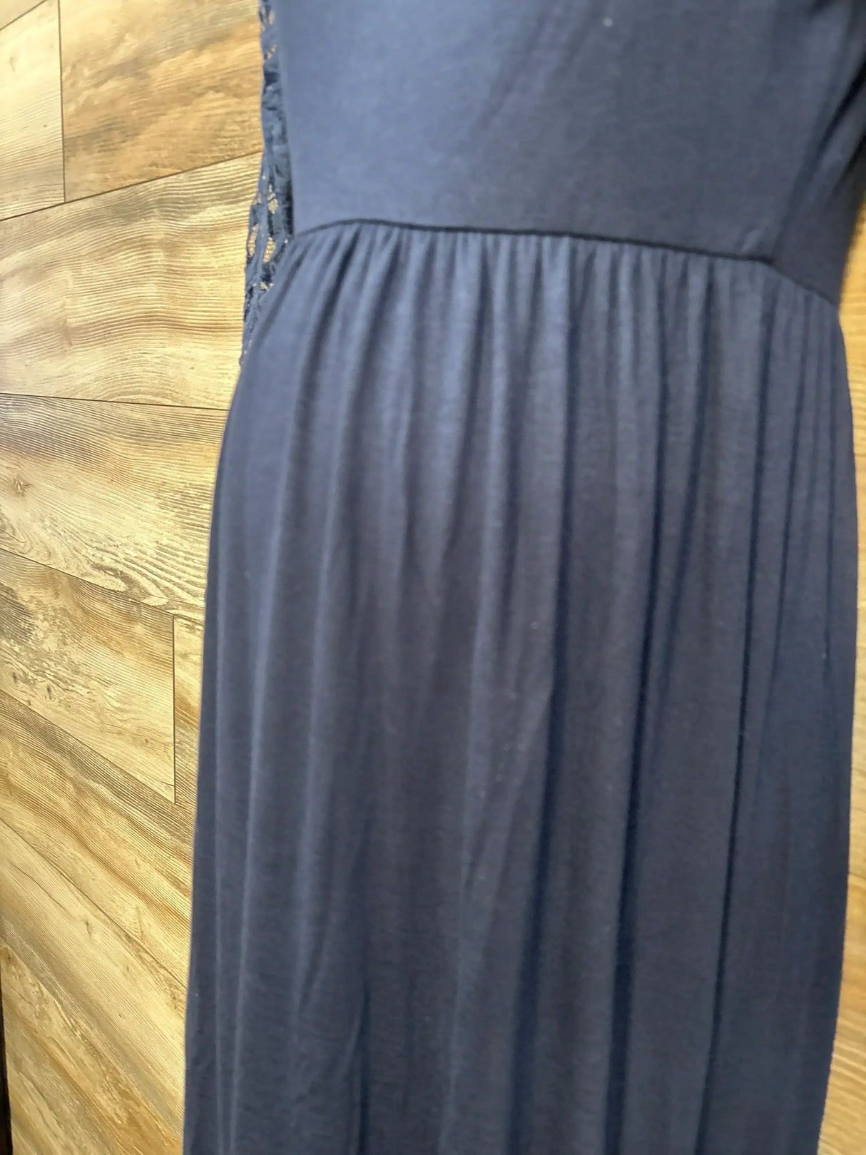 Close-up side view of navy Pink Blush maternity maxi dress showing gathered empire waist and lace side sleeve detail on wood background