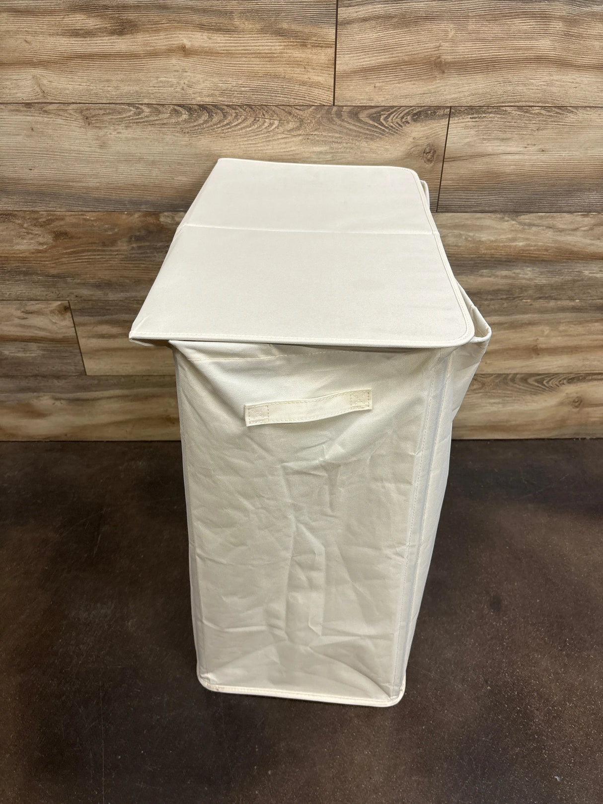 Top-front view of BGTREND double laundry hamper showcasing closed lid and front carry handle with wood-paneled wall and dark floor background